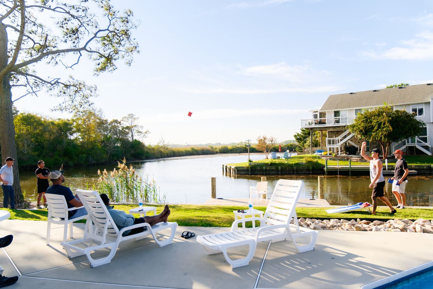 White outdoor plastic lounge chairs line up along a patio area with scenic water views at sunset.