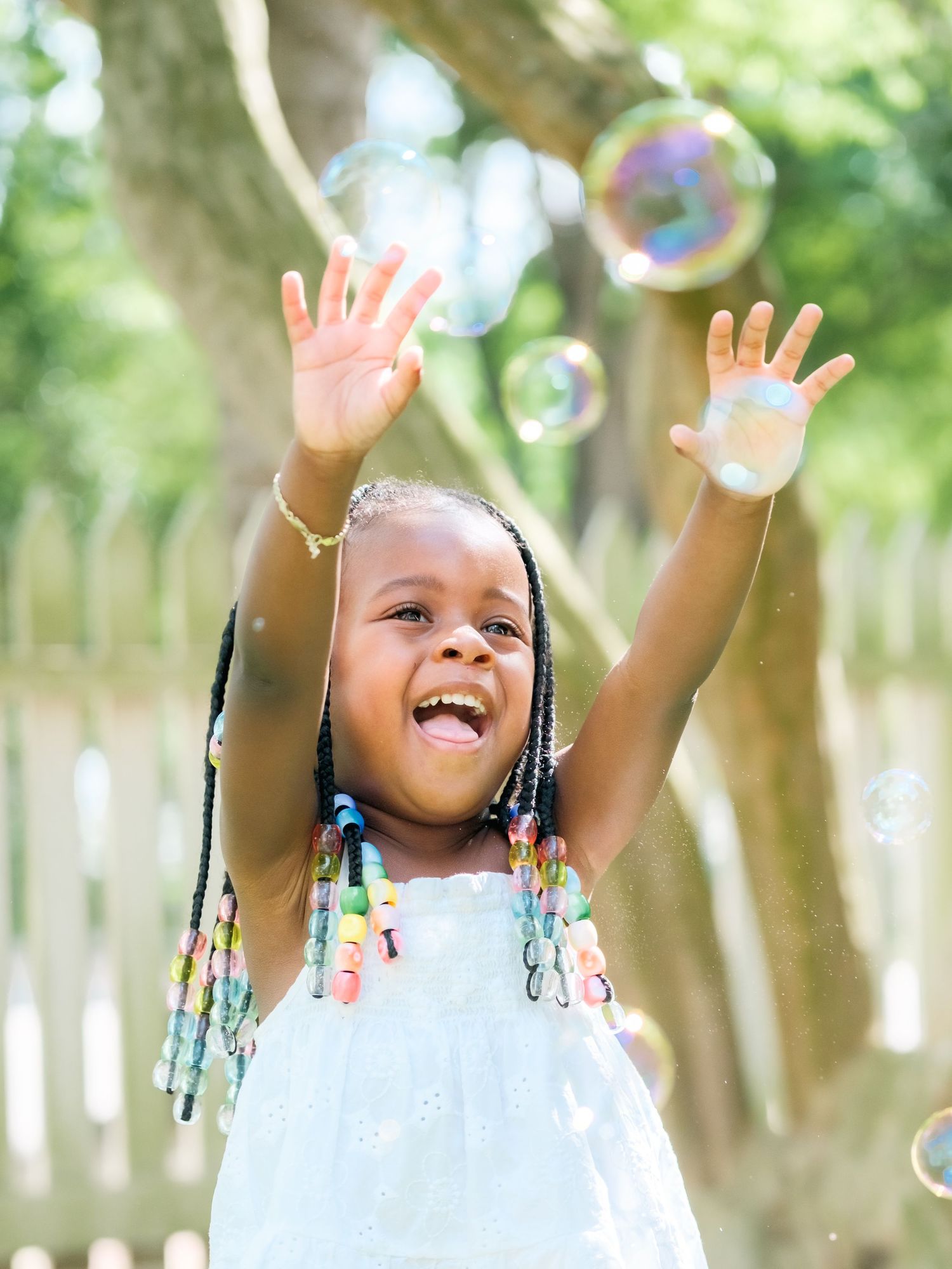 Joyful young person reaching up to catch iridescent soap bubbles while playing outside on a sunny day.