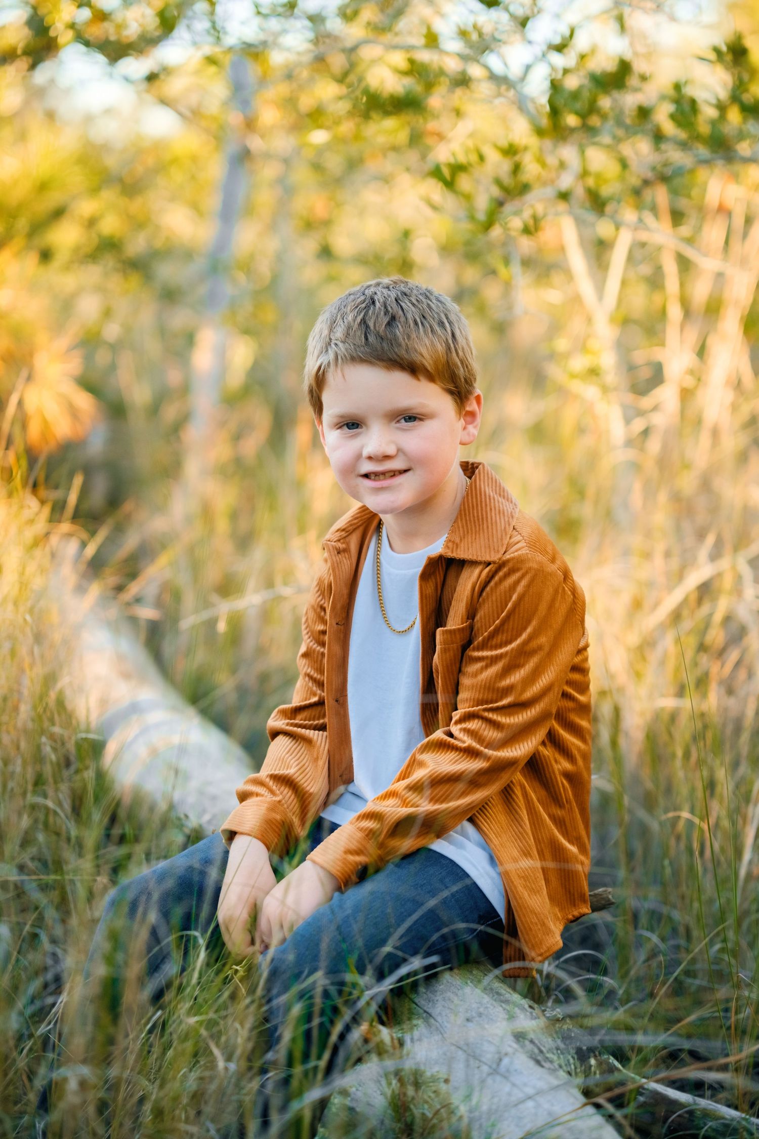 Children sitting in tall grass during golden hour, wearing brown and white outfits against a natural backdrop.