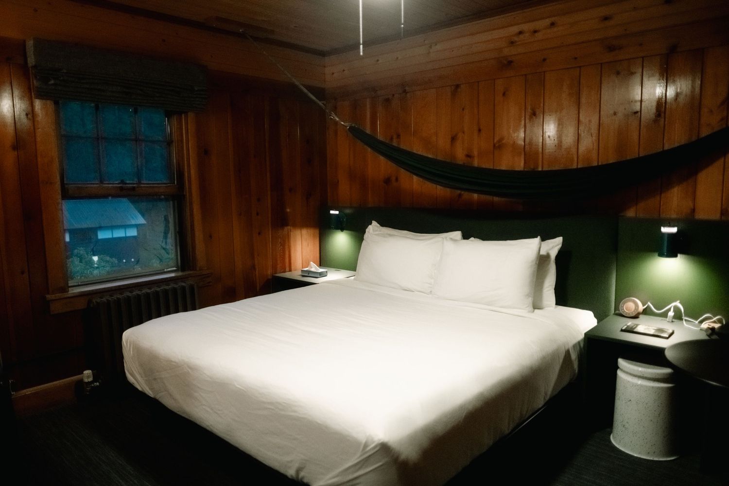 A dark wood-paneled room with modern white bedding and contemporary furniture creates a cozy hotel atmosphere.