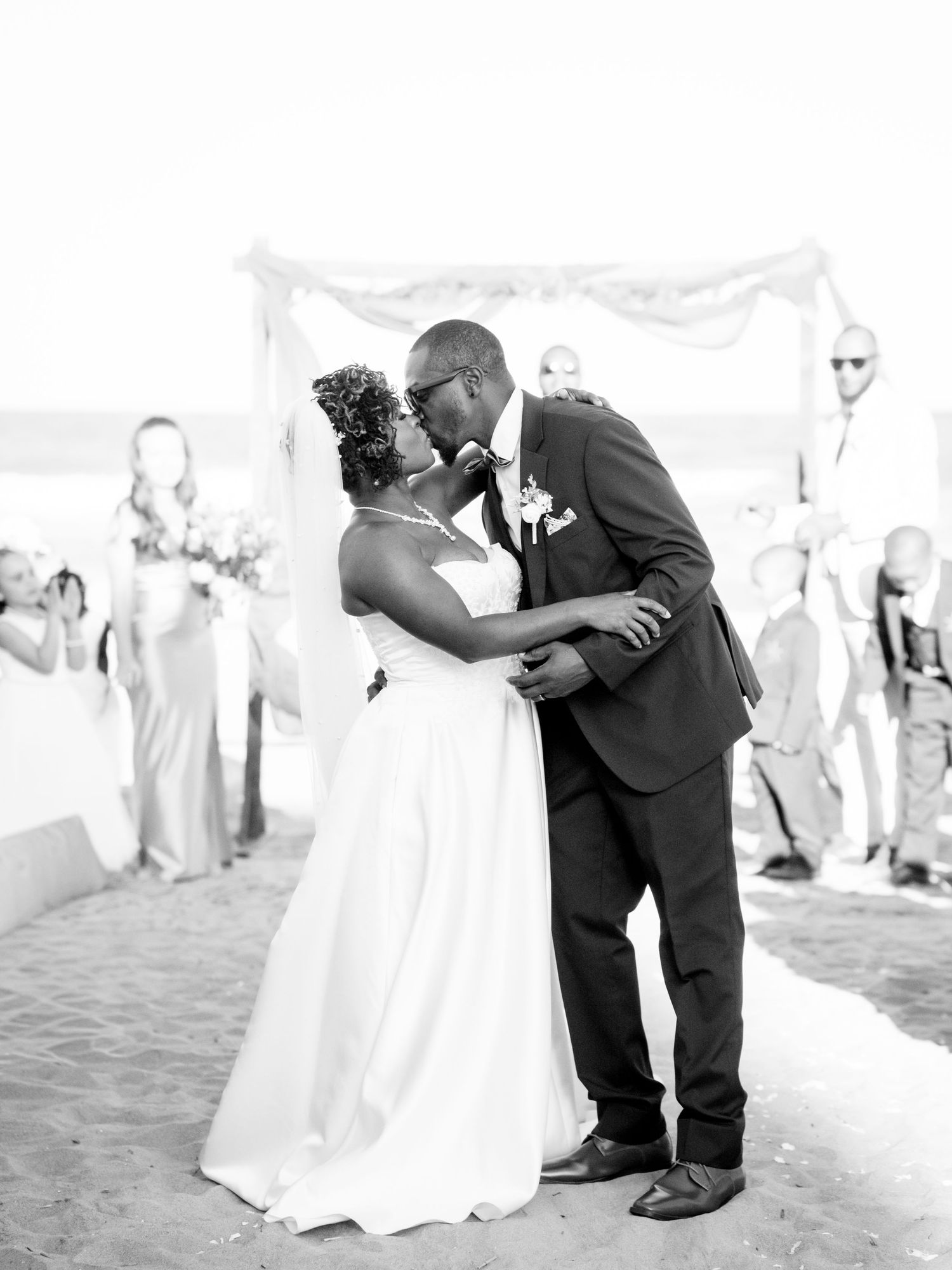 A romantic wedding kiss moment under a white canopy on the beach.