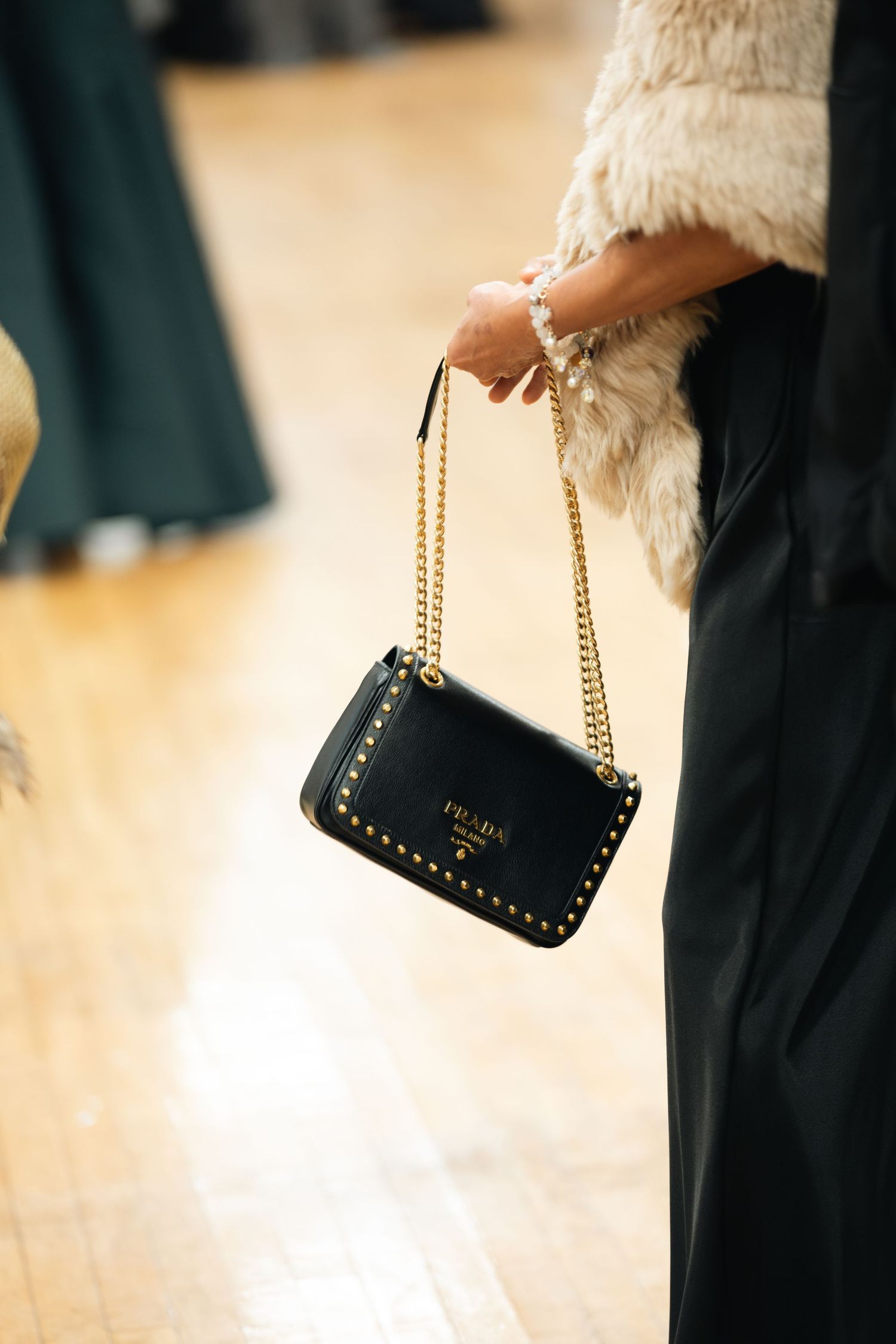 Four closeup photos showing a small black leather studded handbag being held against a blurred beige background.