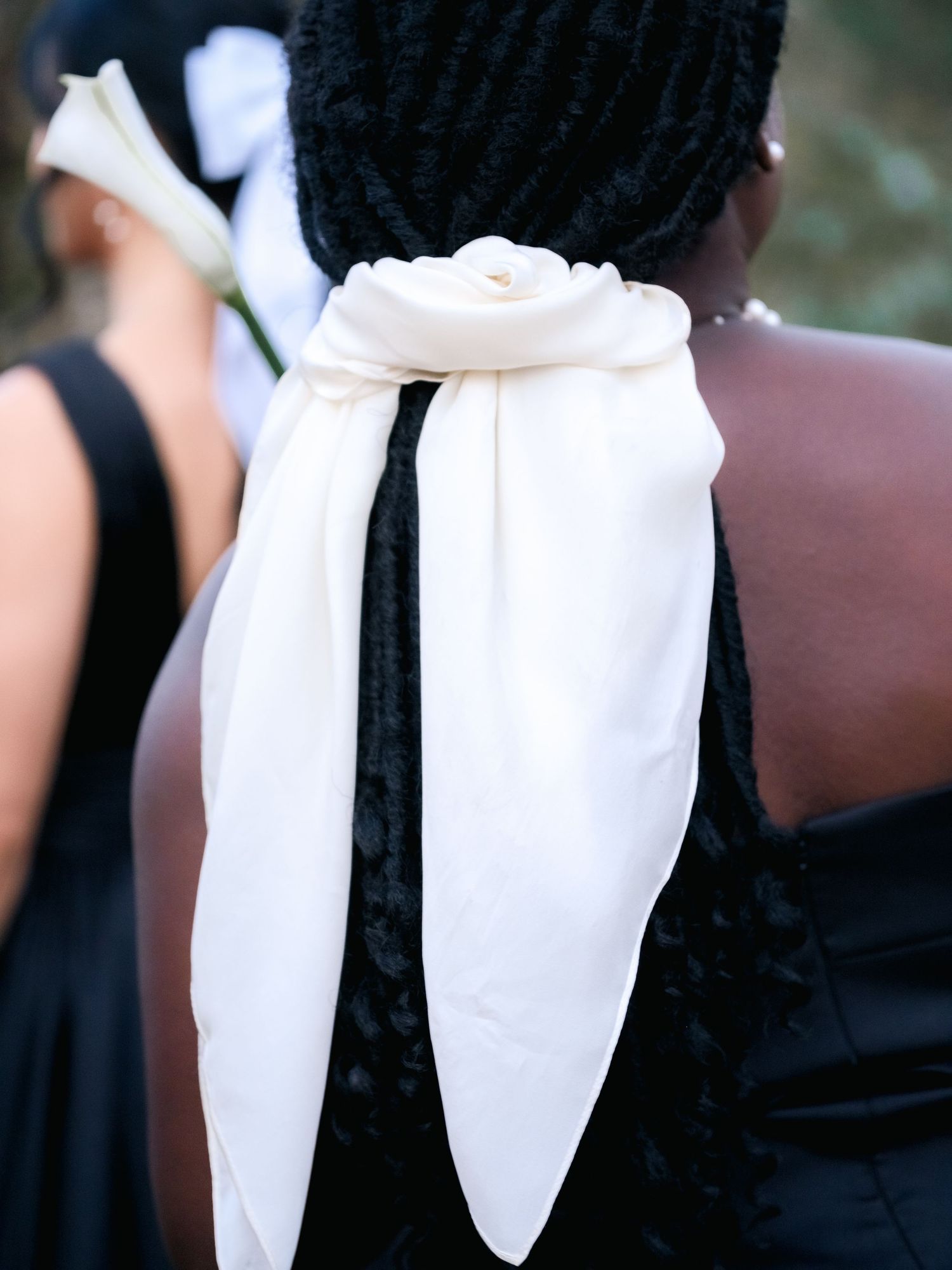 Long braided black hair tied back with an elegant white scarf at the nape of the neck.