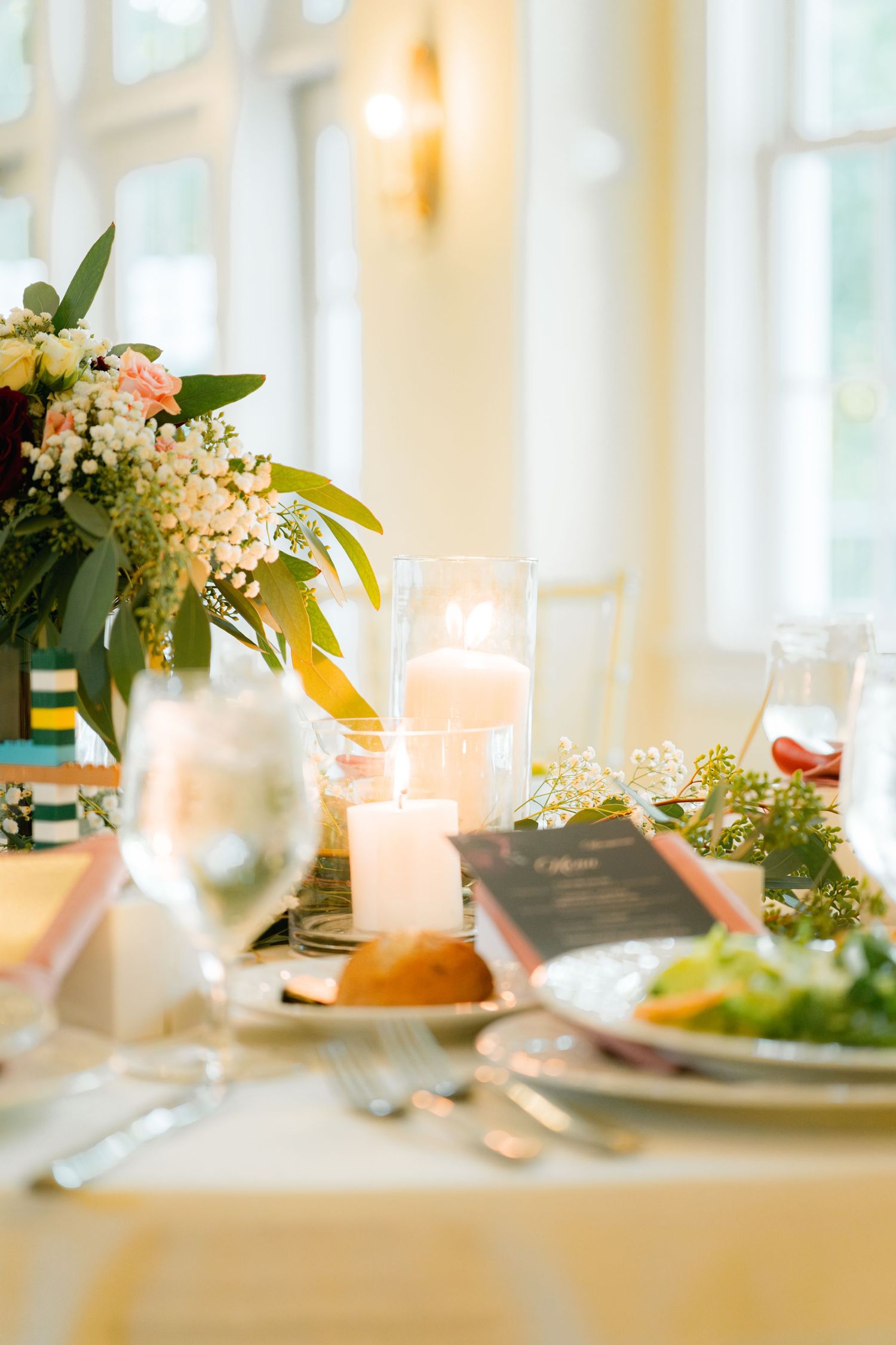 Elegant wedding reception table setting with glowing candles, floral centerpiece and place settings bathed in warm light.