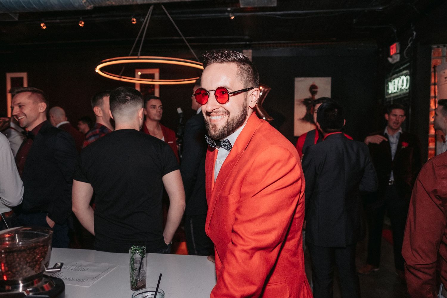 People mingling and socializing at a dimly lit nightclub or bar with red lighting accents.