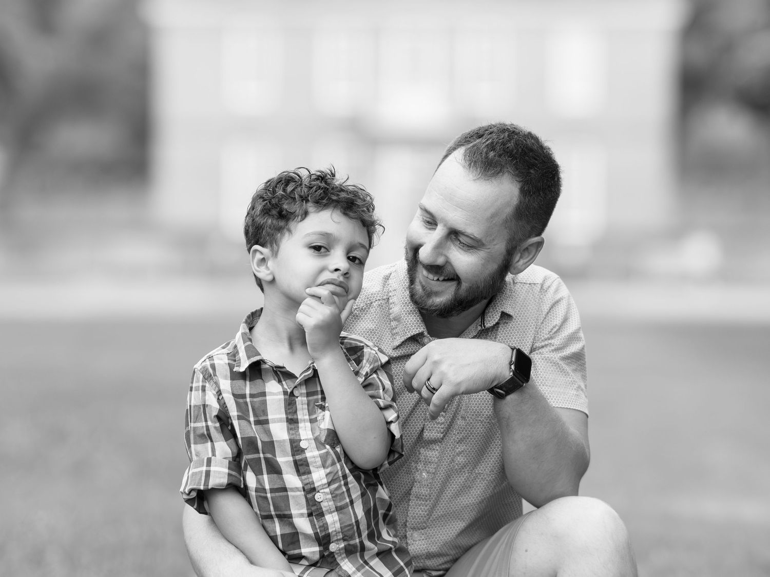 Black and white candid photo of a happy parent and child sharing a playful moment outdoors.