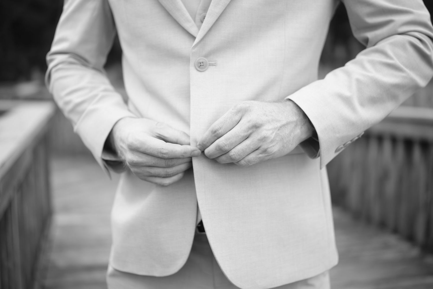 Close-up black and white photo of hands buttoning a white suit jacket.