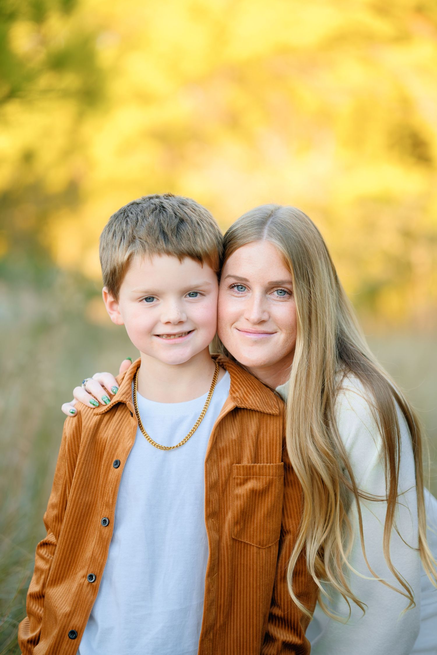 Two siblings pose together outdoors with autumn foliage creating a warm golden background.