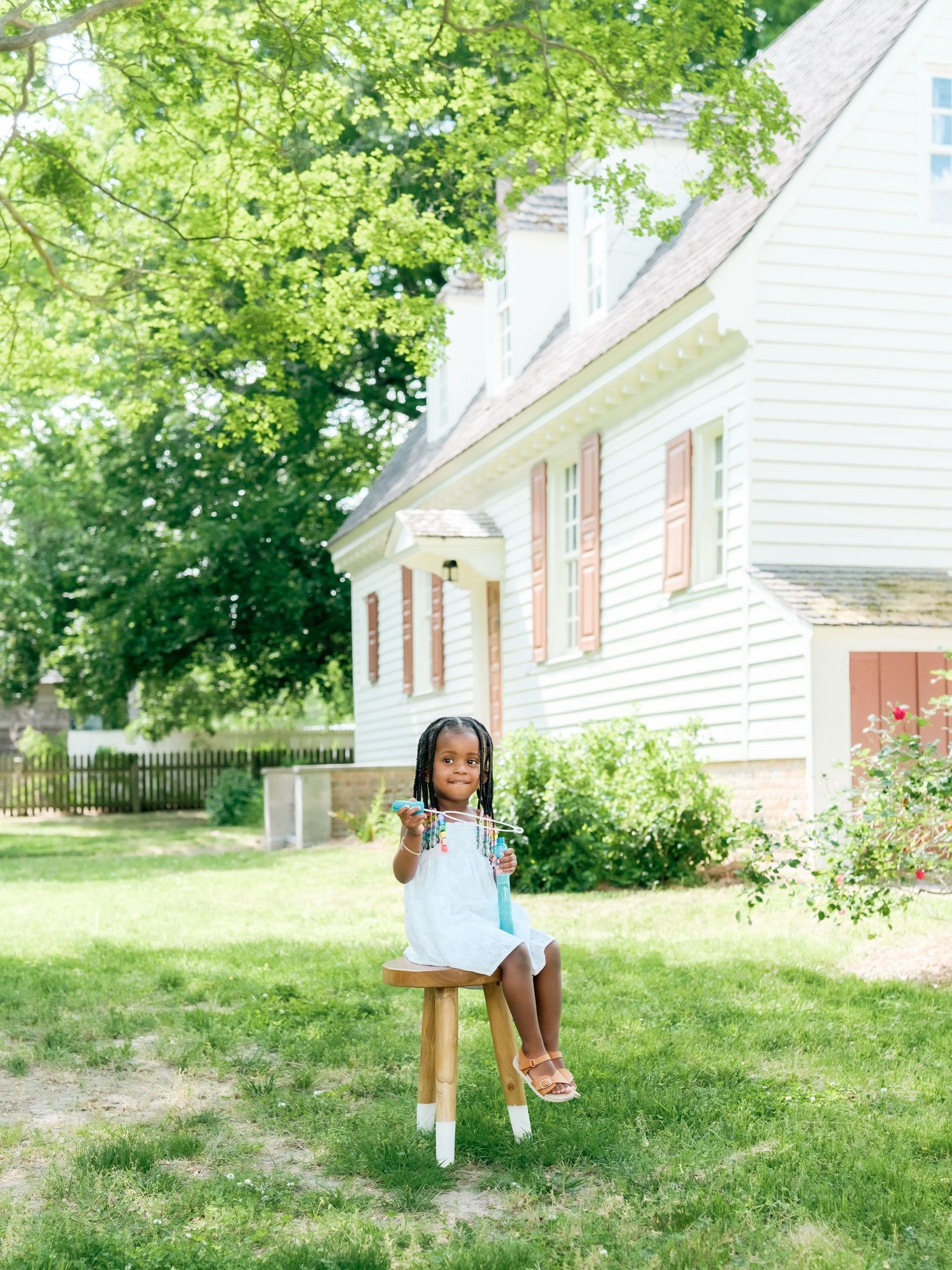 A charming white colonial house with red shutters provides a pastoral backdrop for a summer scene in the green yard.