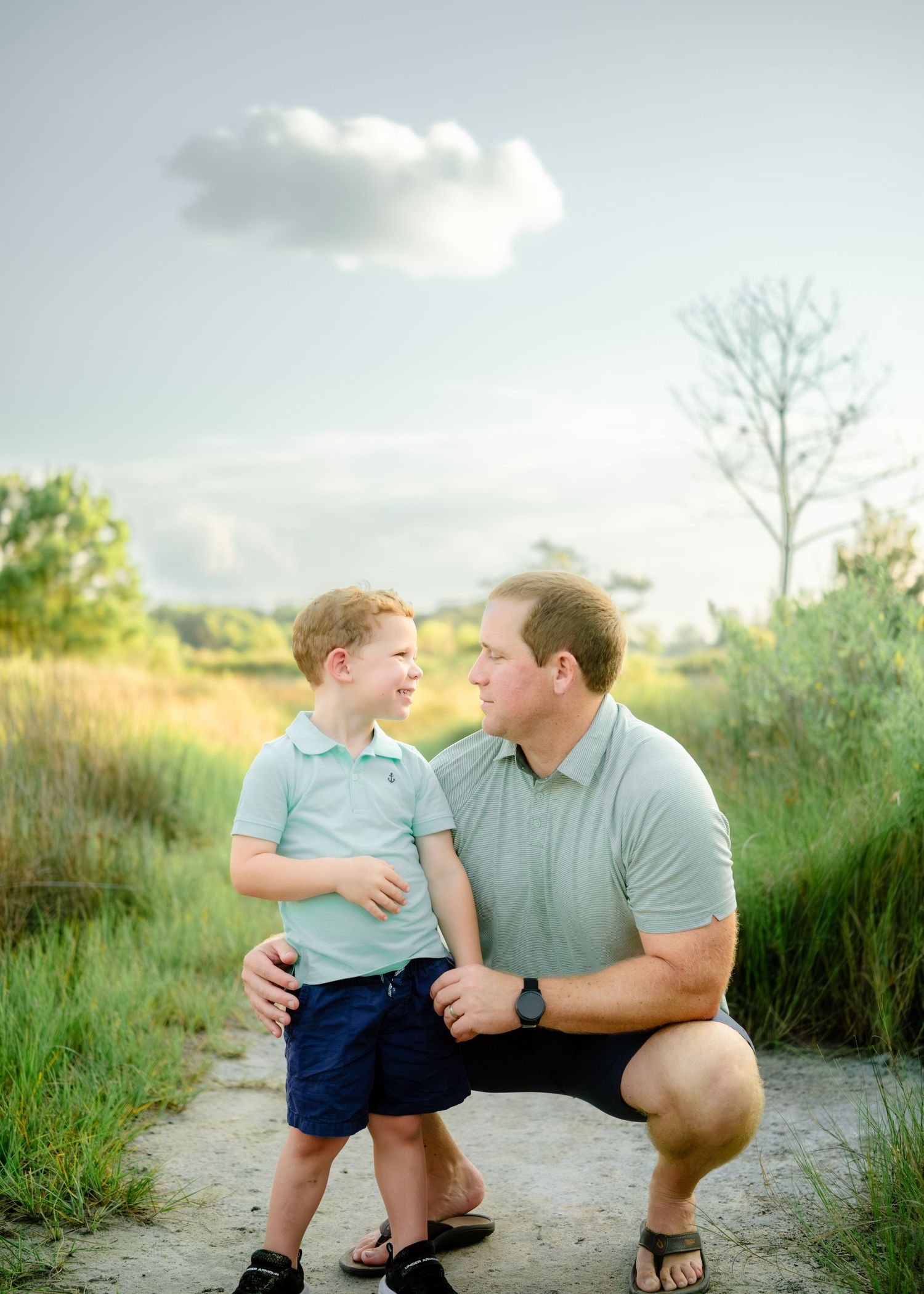 A tender outdoor family moment shared between parent and child on a dirt path surrounded by natural greenery.