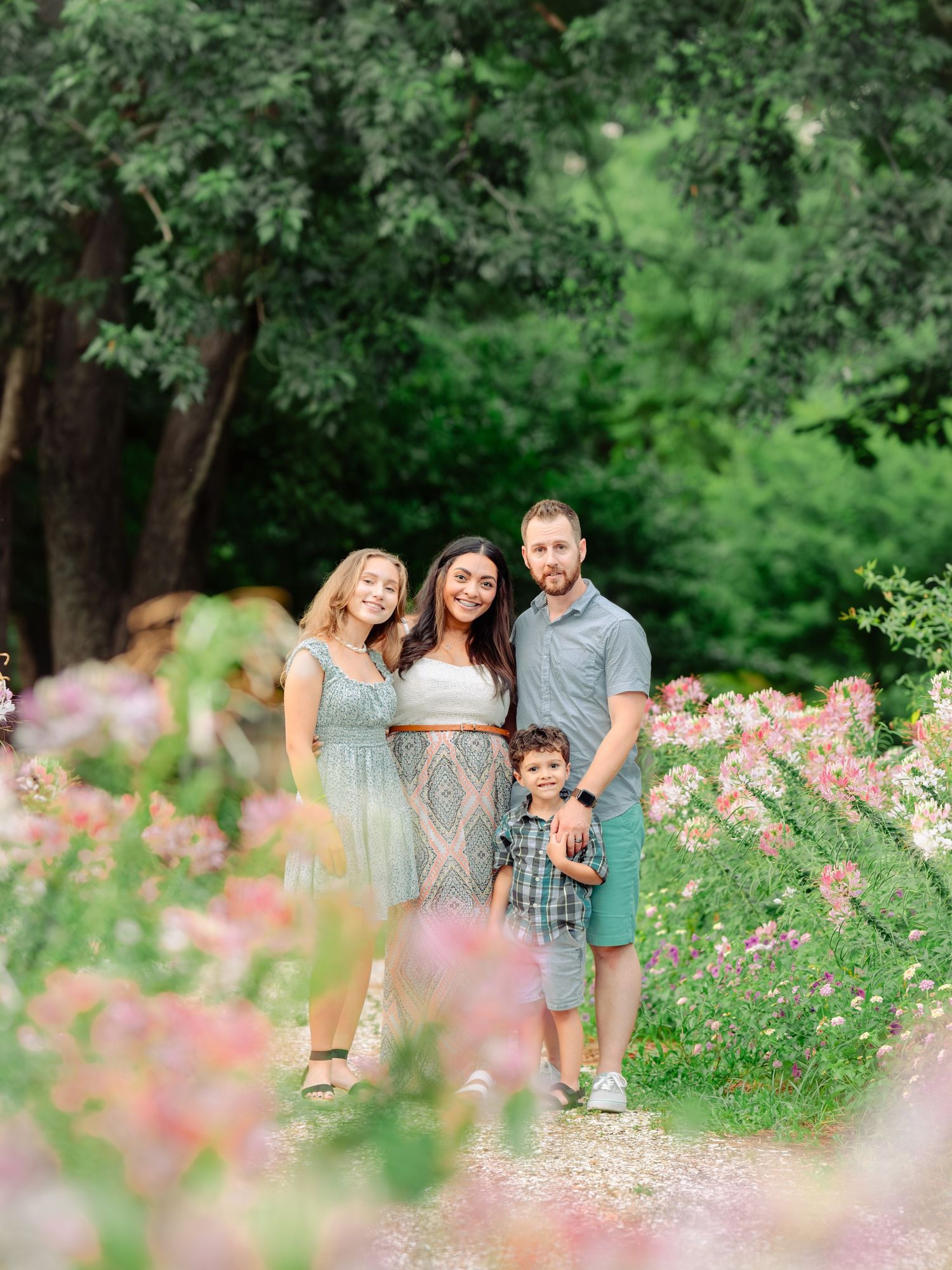 A family relaxes and poses together in a lush garden setting with blooming pink cosmos flowers in the foreground.