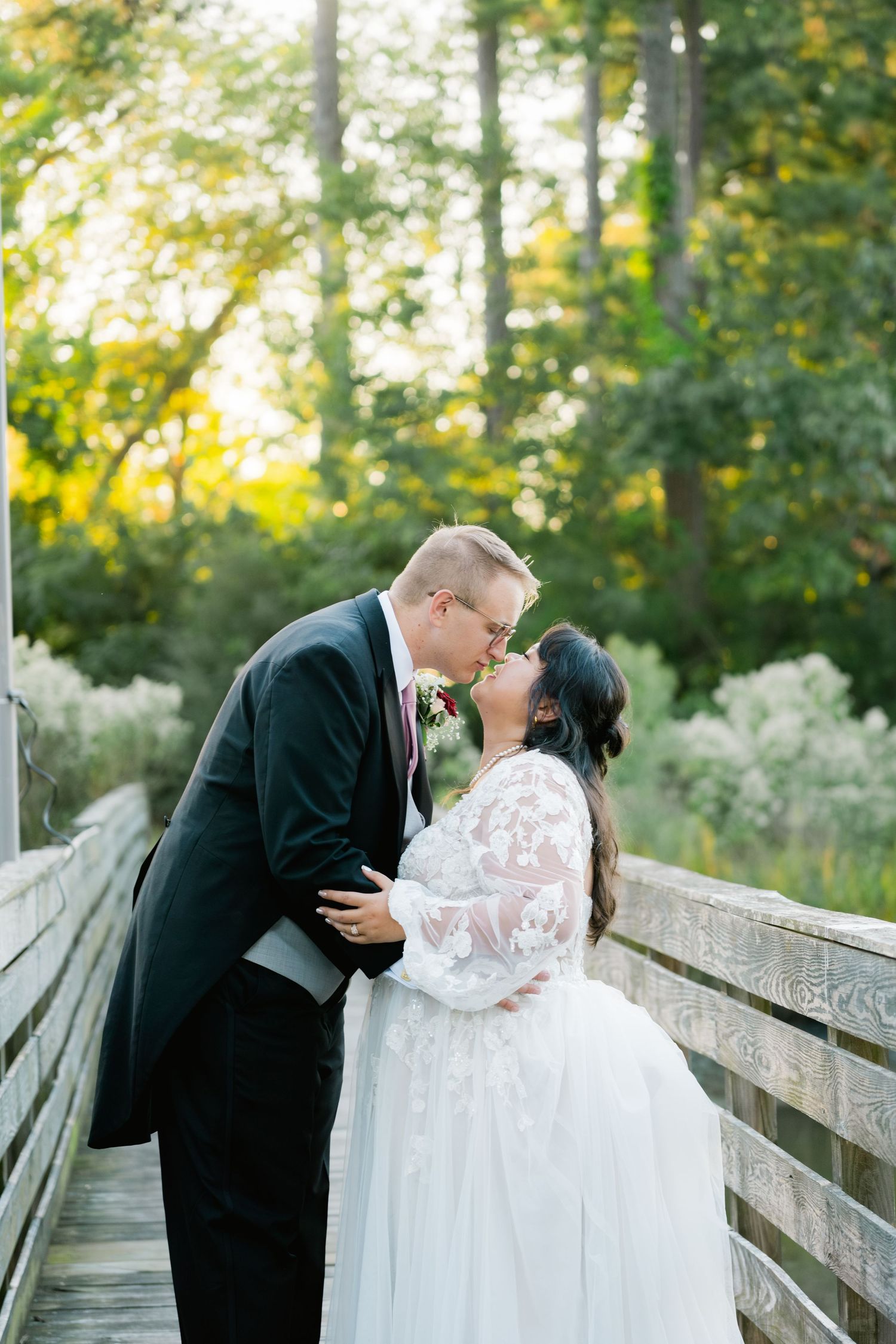 A romantic wedding couple sharing an intimate moment on a wooden bridge surrounded by lush greenery.