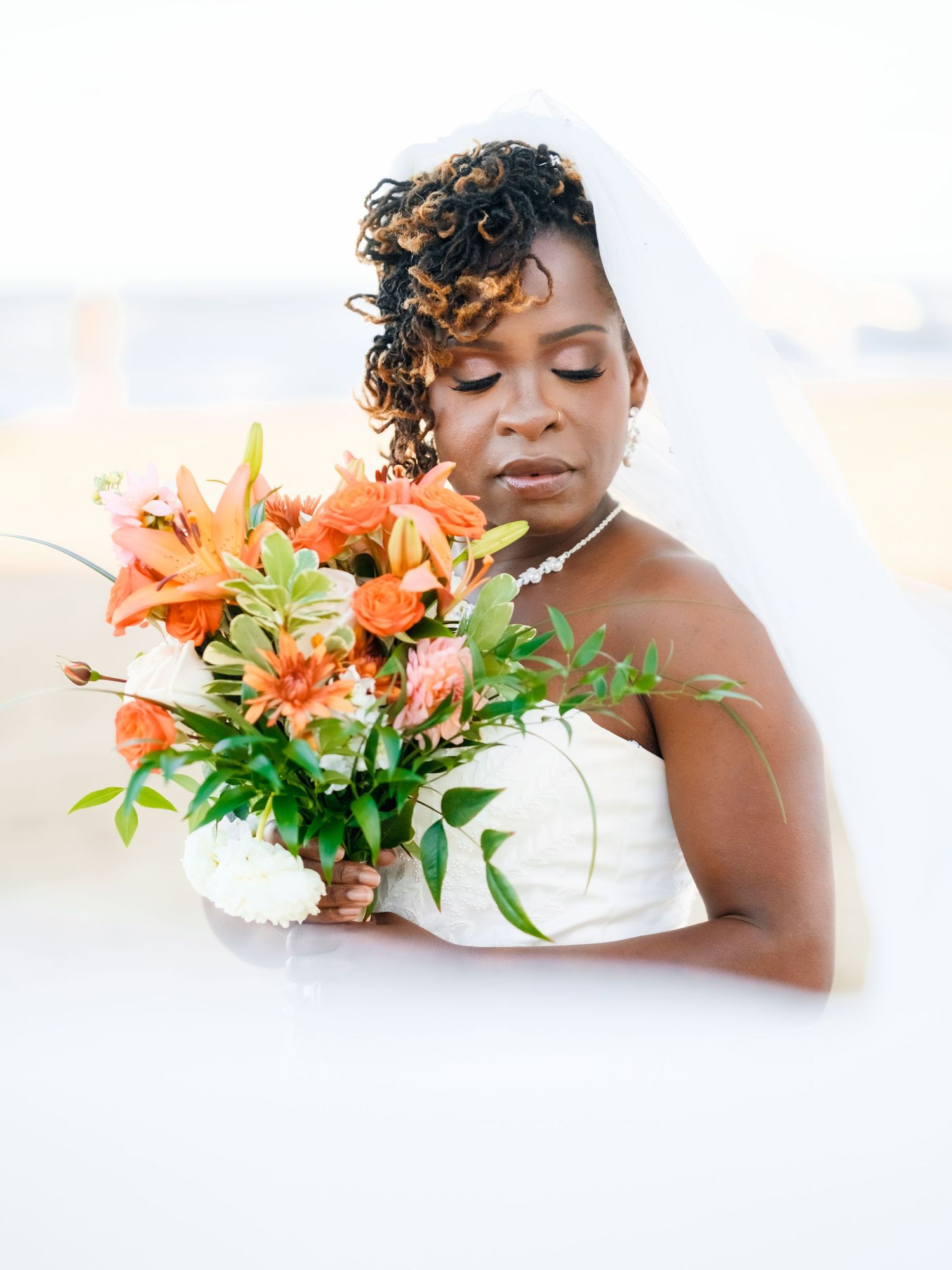 Artistic bridal portrait with orange lilies and white flowers creating a dreamy composition.