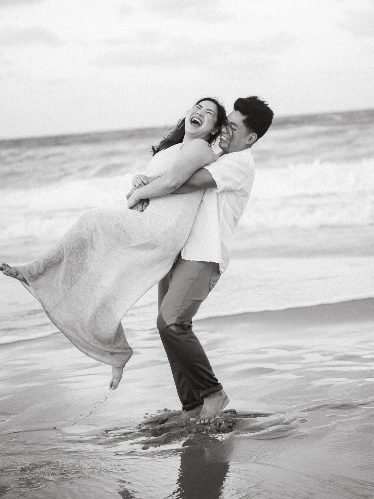 A couple plays in the ocean waves at the beach, creating a series of joyful black and white romantic moments.