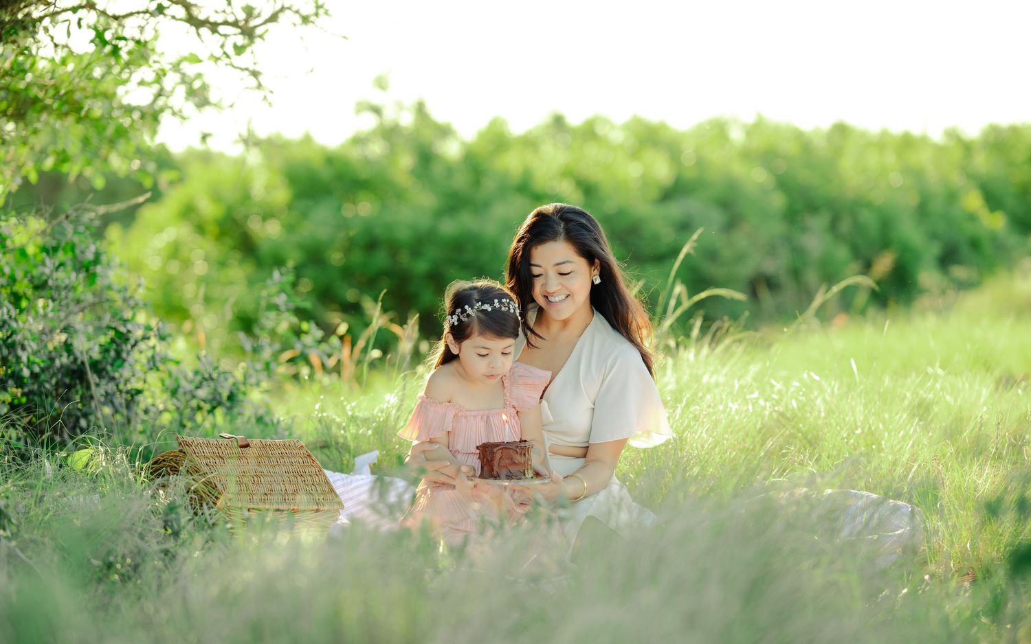 A couple sits among wildflowers in a sunny meadow with warm golden light filtering through green grass.