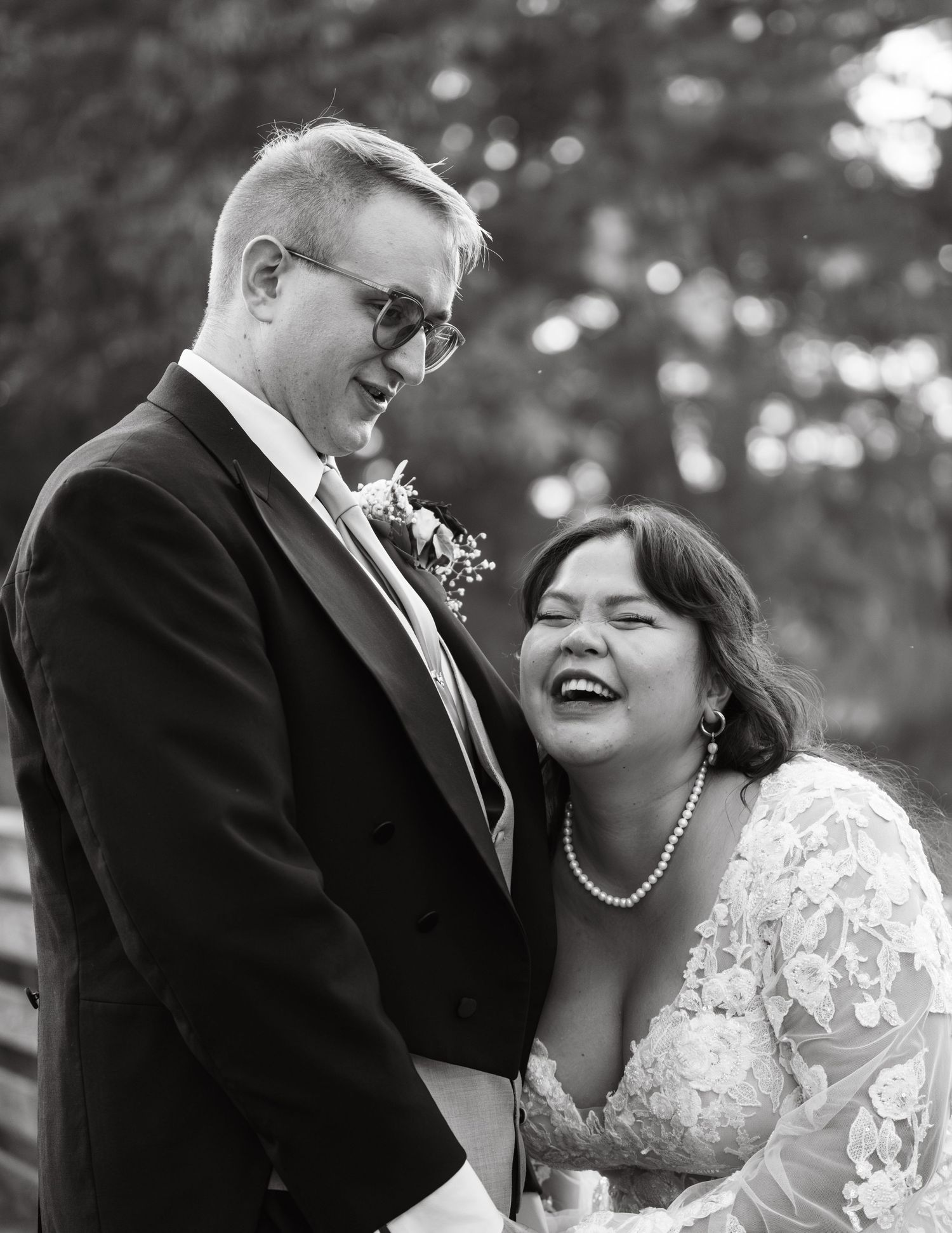 A black and white candid wedding photo shows a couple sharing a joyful moment together outdoors.