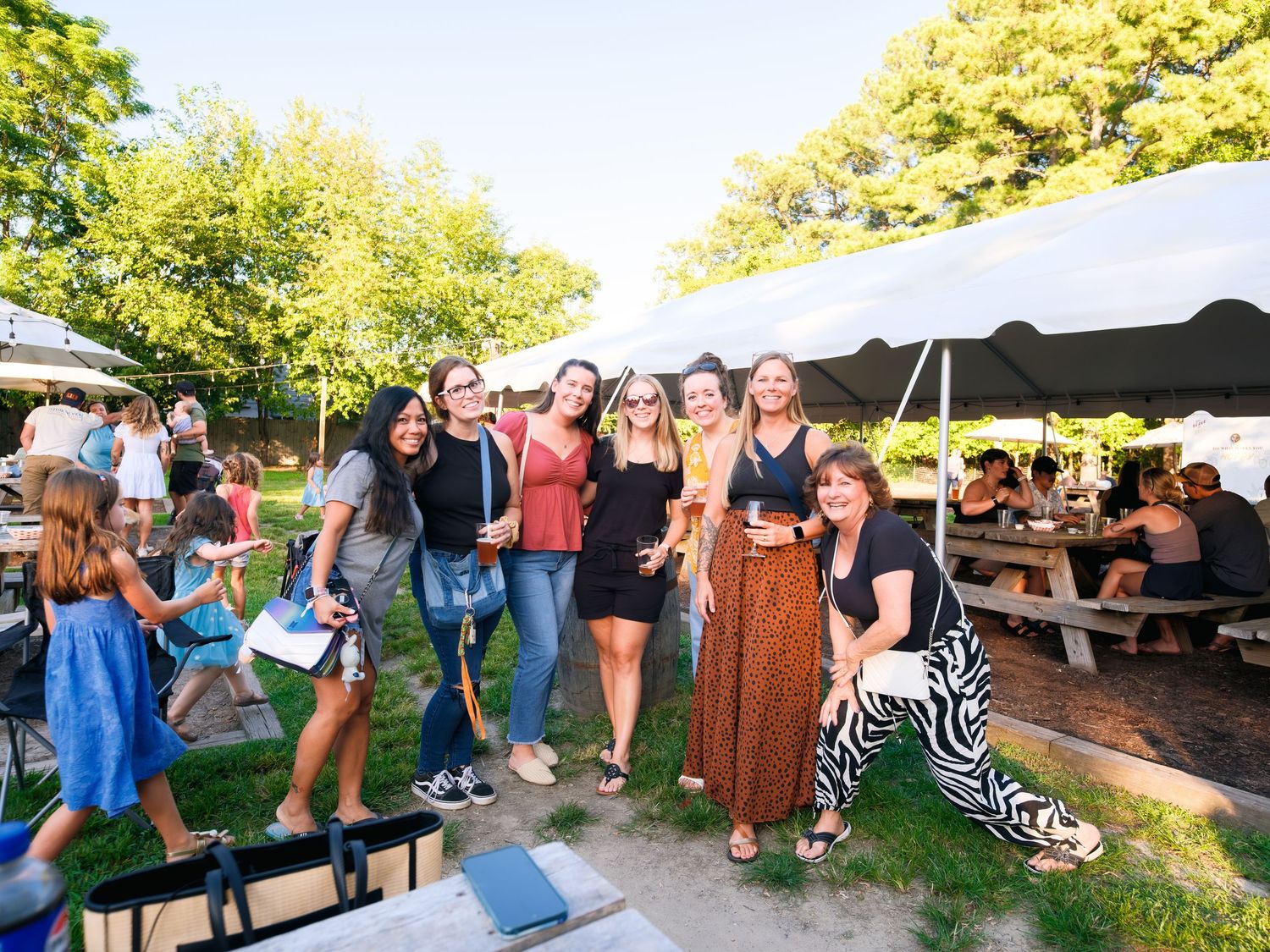 People gathered at outdoor picnic tables enjoy food and drinks during a summer event.