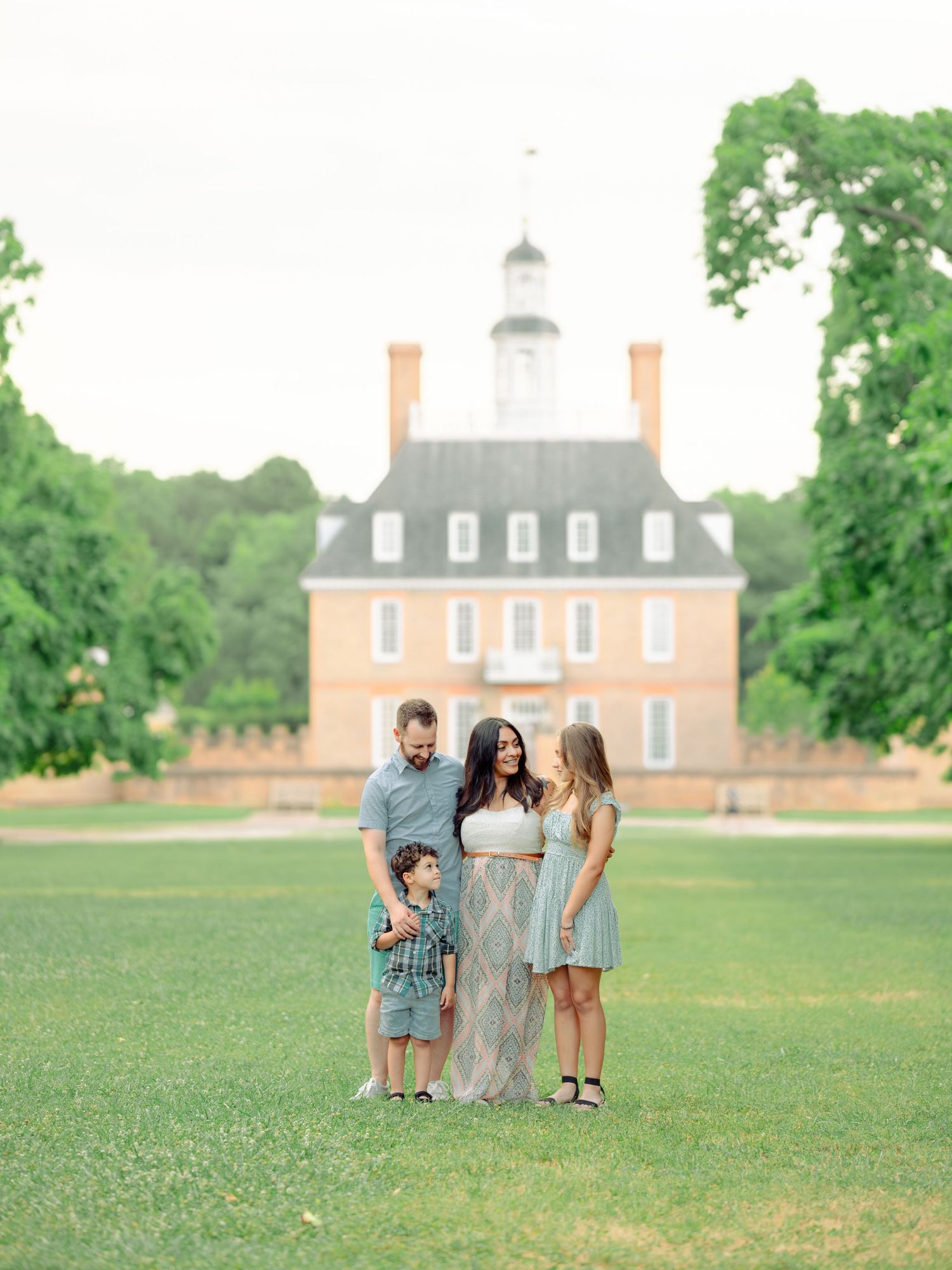 A family stands on the lush green lawn in front of the historic Governor's Palace at Colonial Williamsburg.