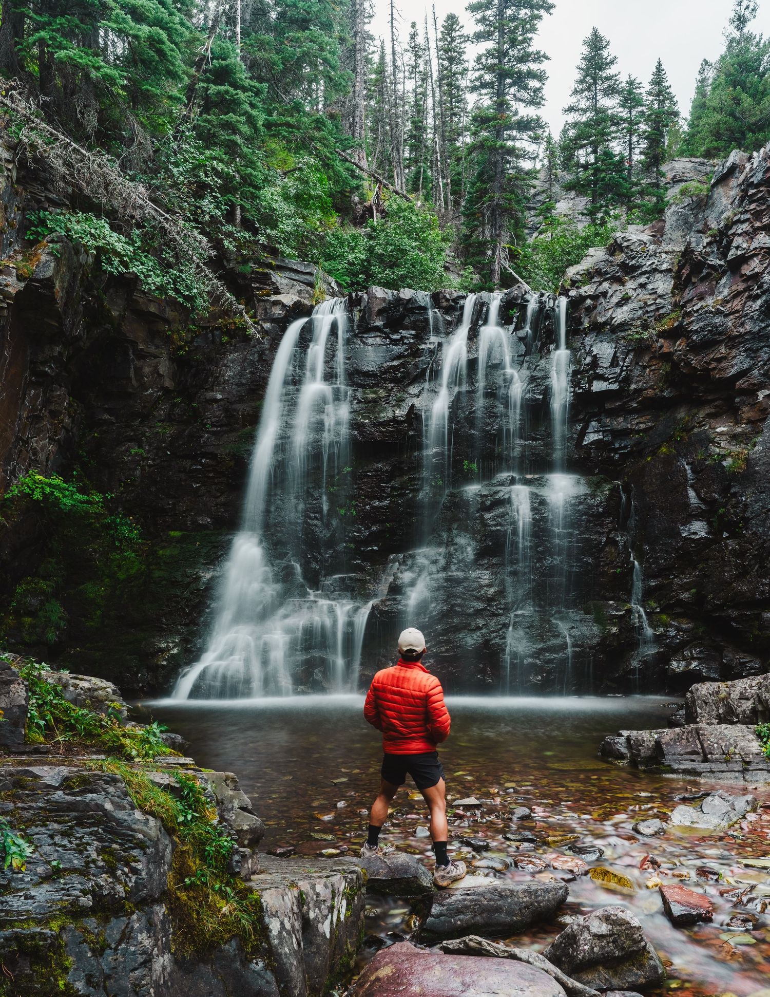 A tranquil waterfall cascades down dark rocky cliffs surrounded by lush evergreen forest in multiple scenic views.