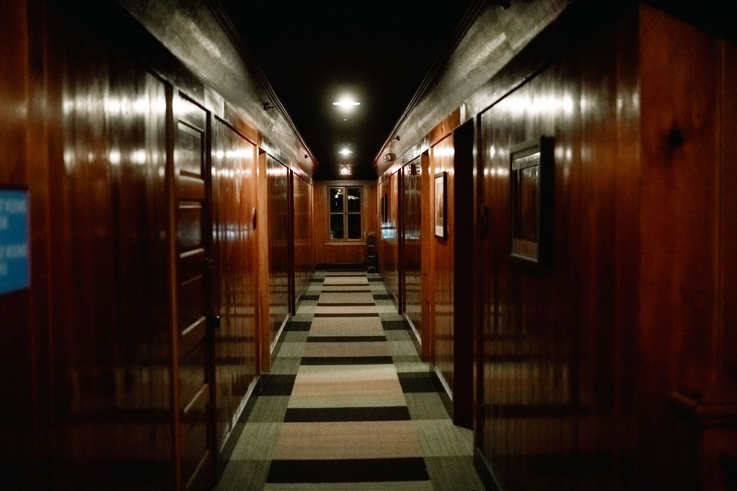 Long dark corridor in a cruise ship with rich wooden paneling and doors leading to passenger cabins.