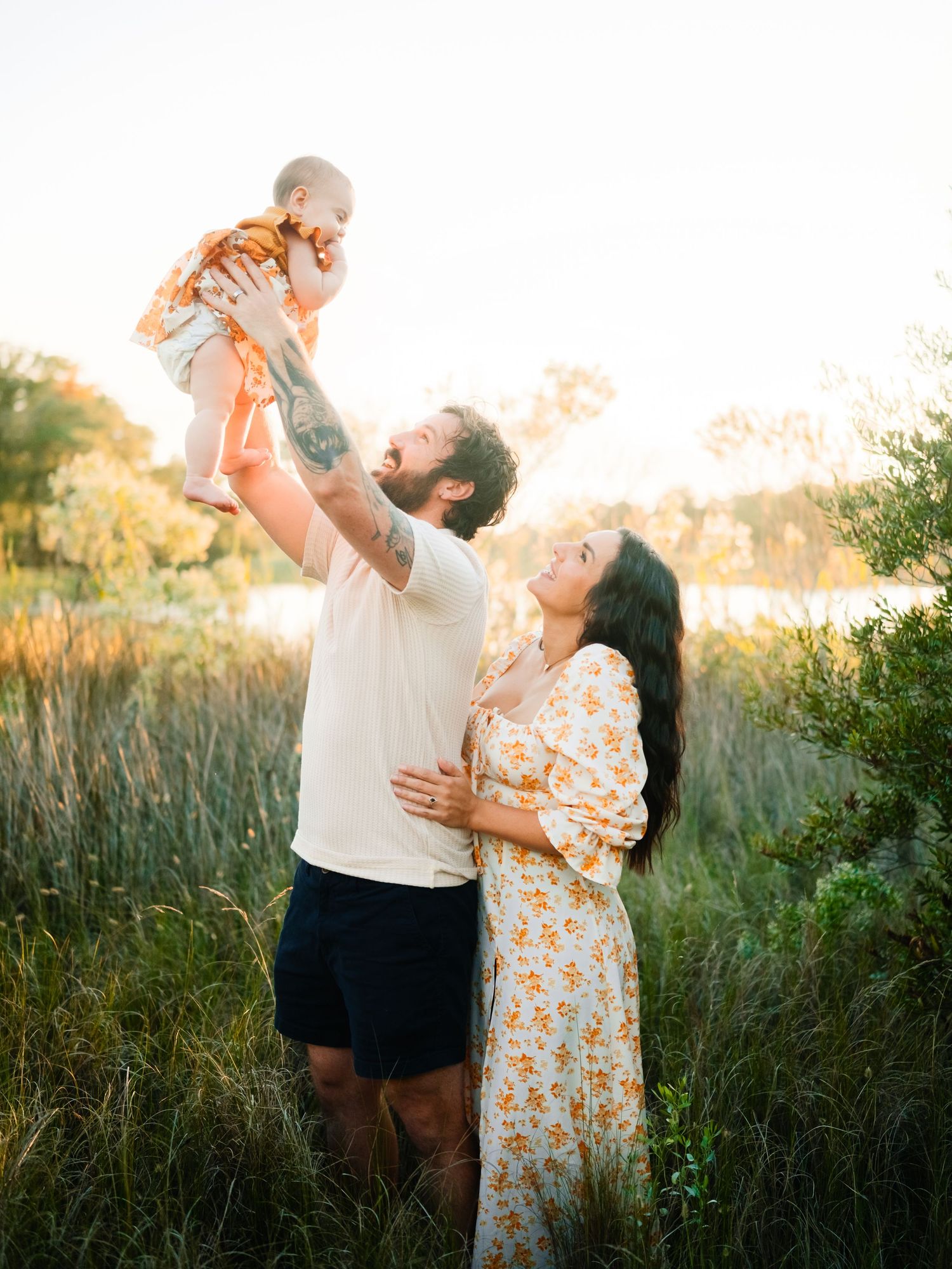 A family enjoys a tender moment together in a sunlit field of tall grass during golden hour.