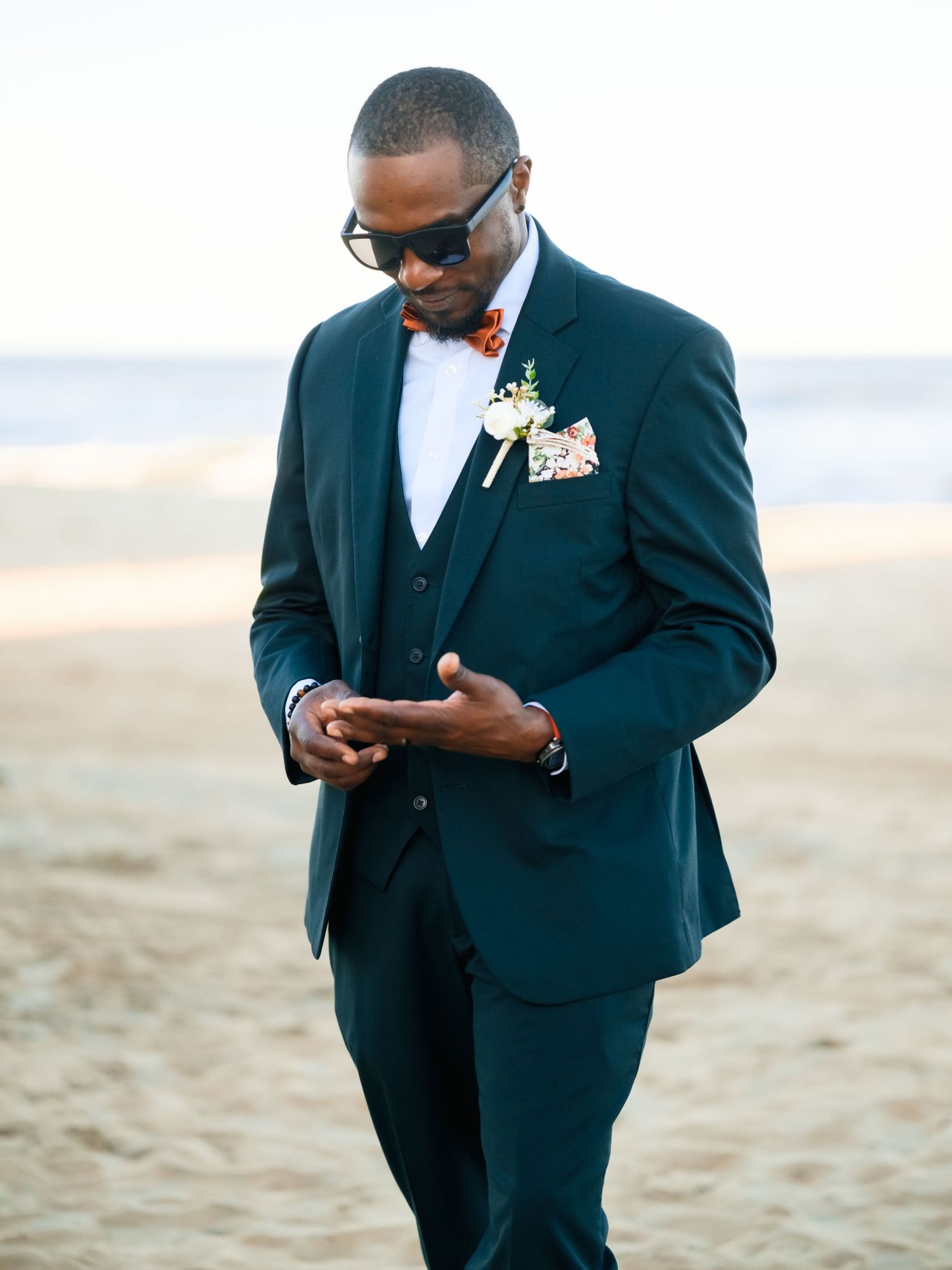 A person in a black suit looking down at their phone while standing on a beach.