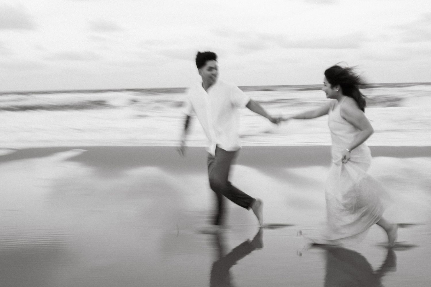 A playful black and white sequence shows two people running and chasing each other along a misty beach shoreline.