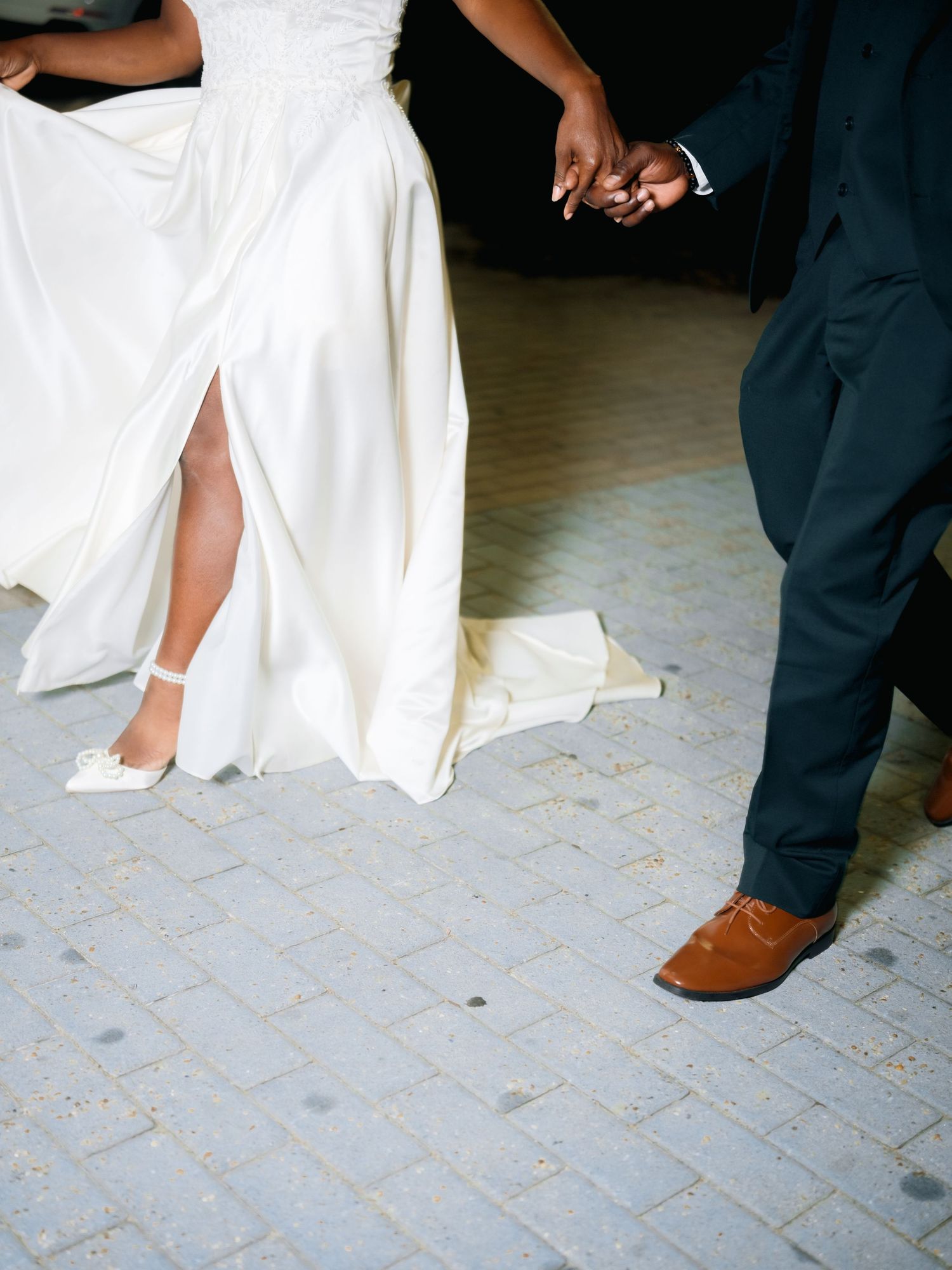 A close-up of a wedding couple's feet showing a white bridal gown and brown dress shoes on a tiled floor.