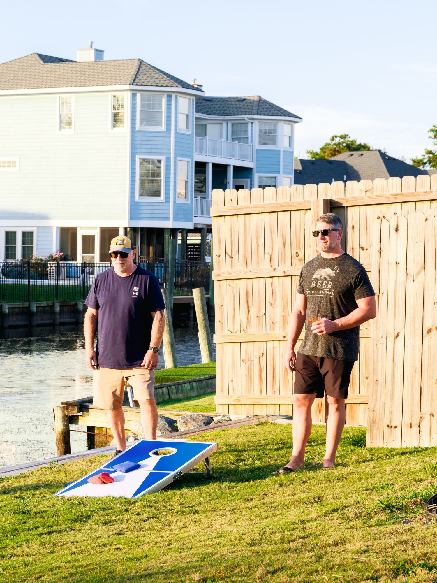 Person playing cornhole on a grassy lawn by waterfront houses shown in a sequence of throwing motion shots.