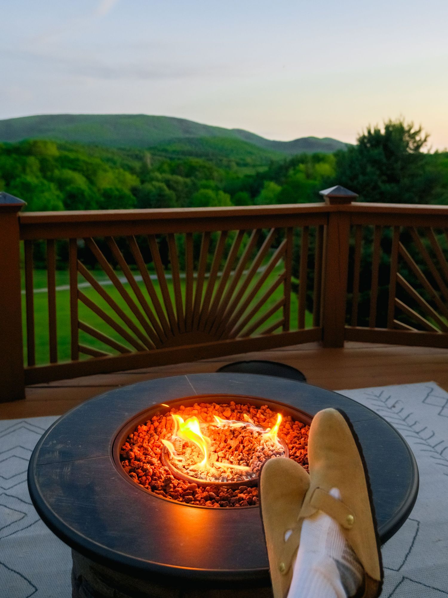 Relaxing view of mountain scenery from a deck with feet up next to a glowing fire pit at dusk.