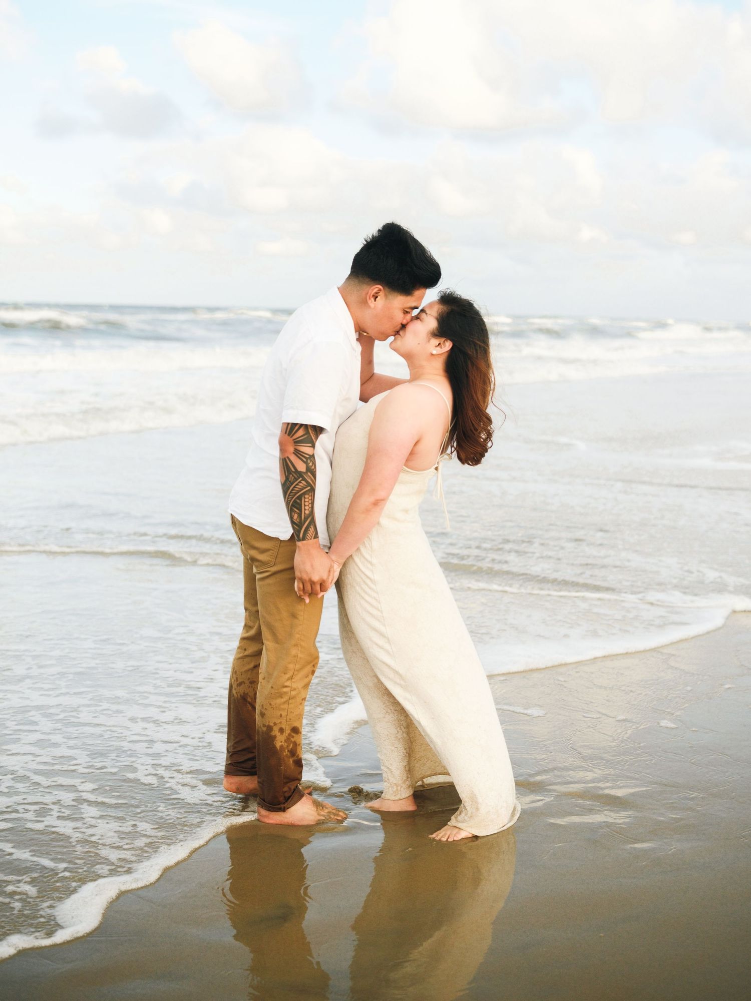 Couple in romantic ocean photoshoot with waves crashing behind them.