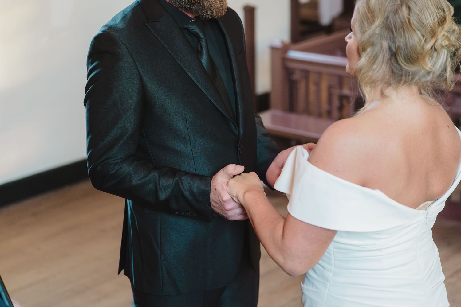 Close up view of hands clasped between two people in formal wedding attire during an intimate ceremony moment.