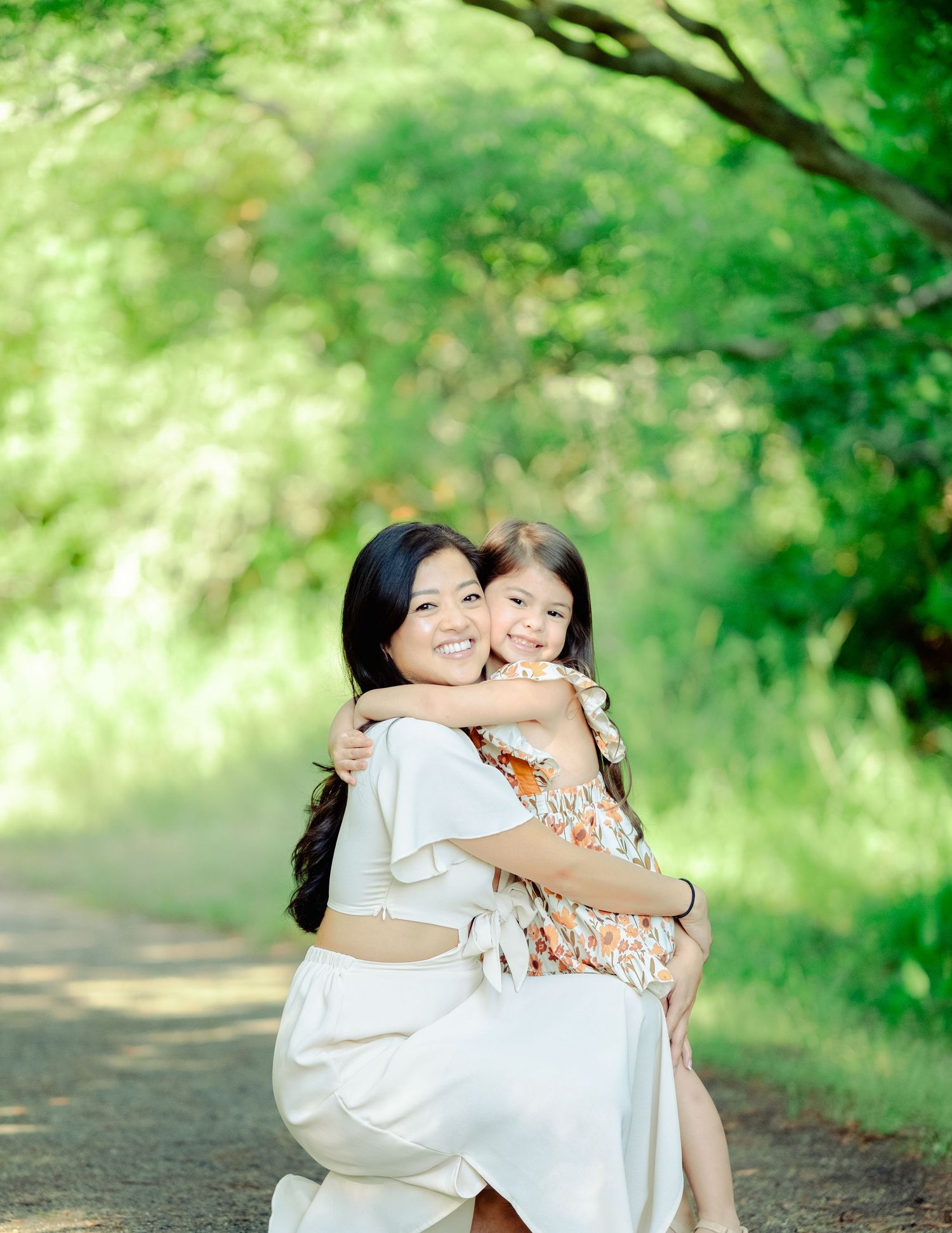 A tender moment shared between two people hugging and laughing together on a path surrounded by lush green foliage.