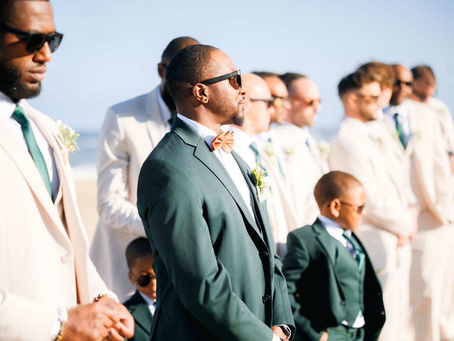 Groomsmen in sunglasses wearing white and green suits stand together outdoors.