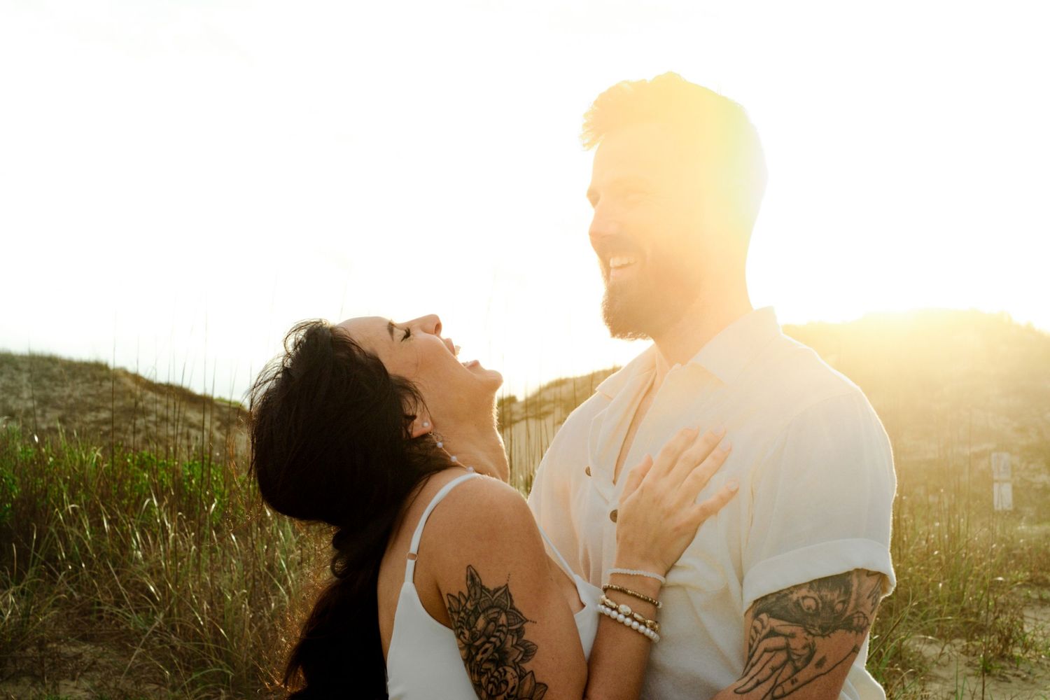 A couple embraces in a sunny meadow during golden hour as sunlight illuminates them from behind.