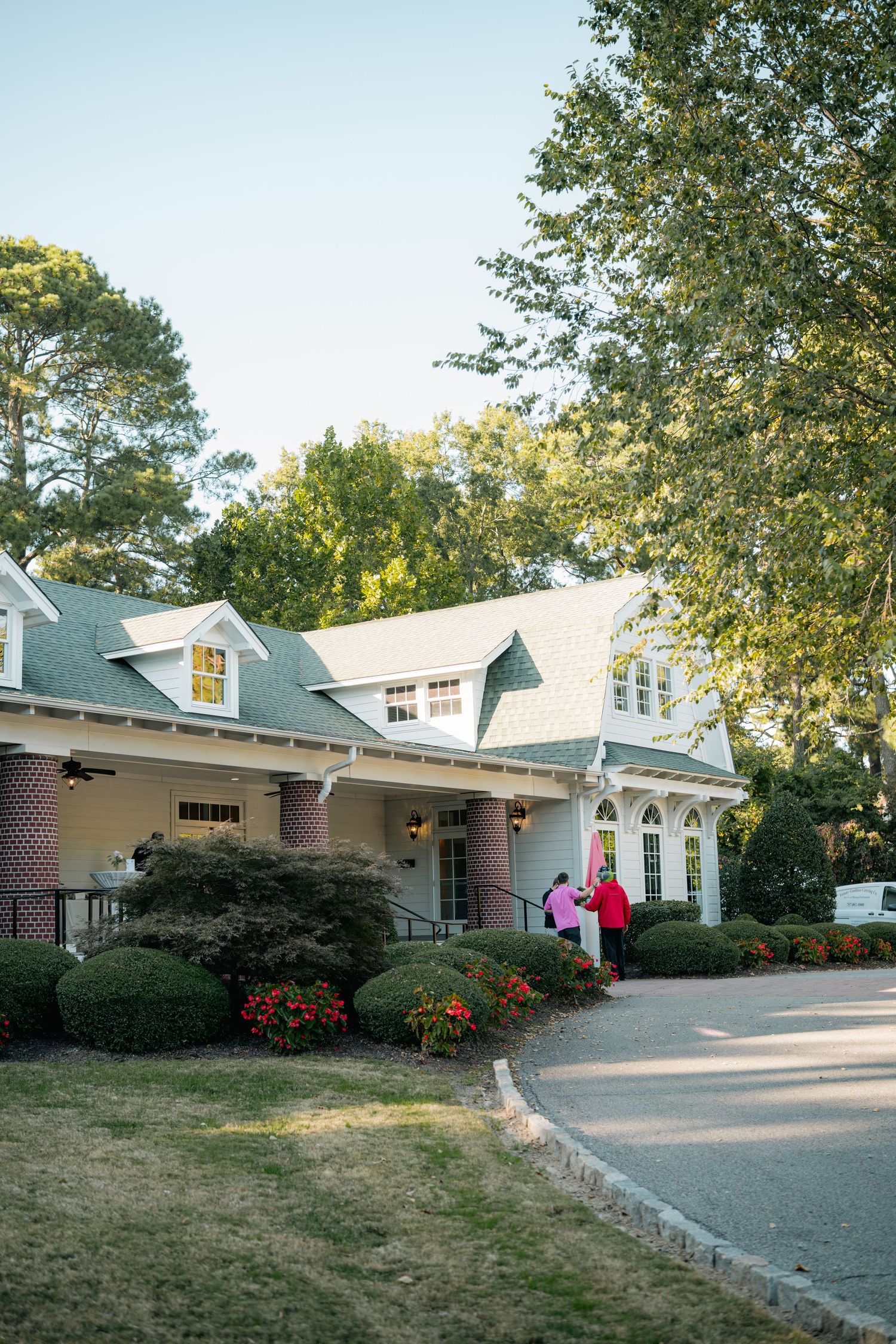 Single-story white building with dormers and brick accents connected by a curved driveway in a leafy suburban setting.