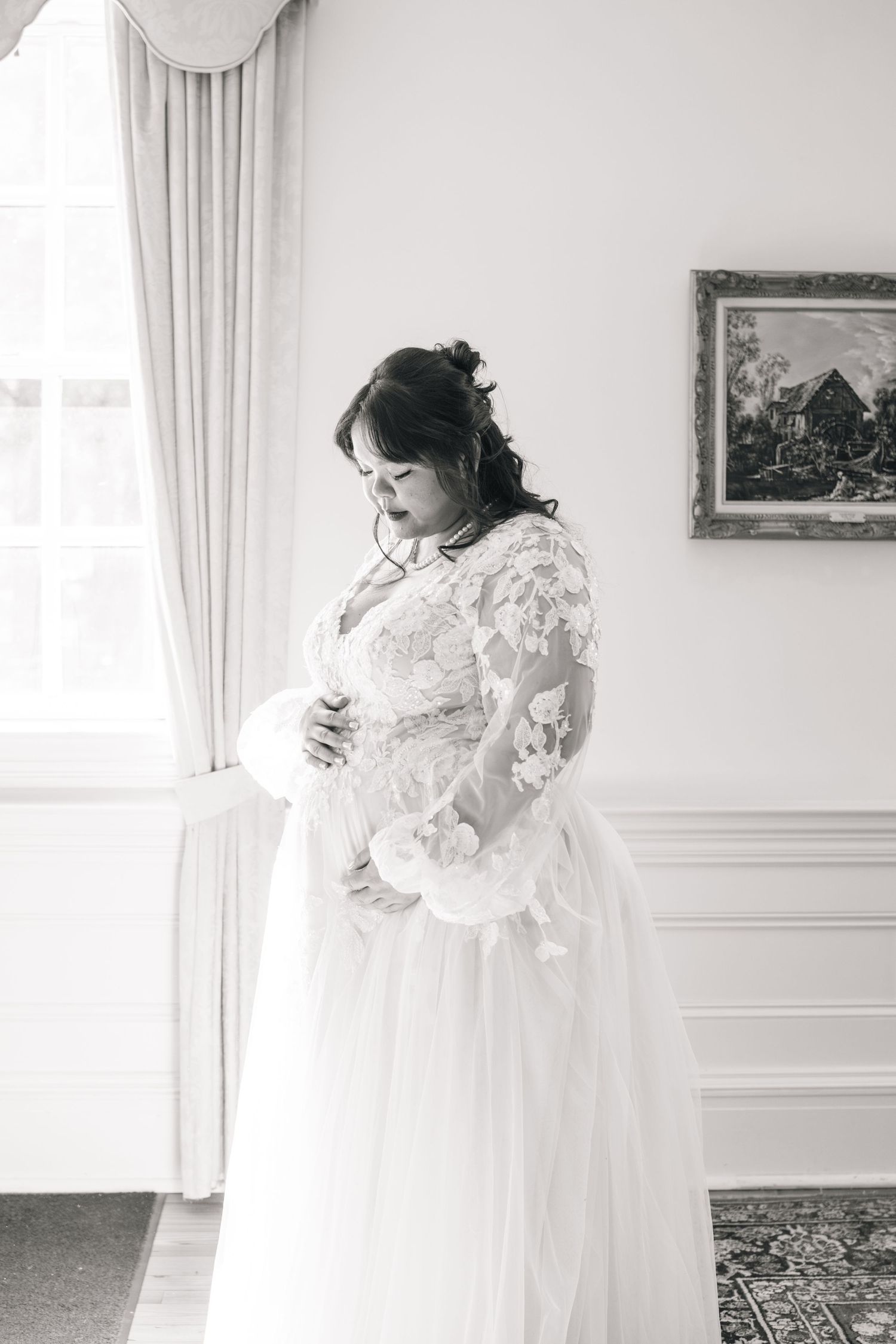 A female wearing a flowing white lace dress in an elegant room with soft window light.