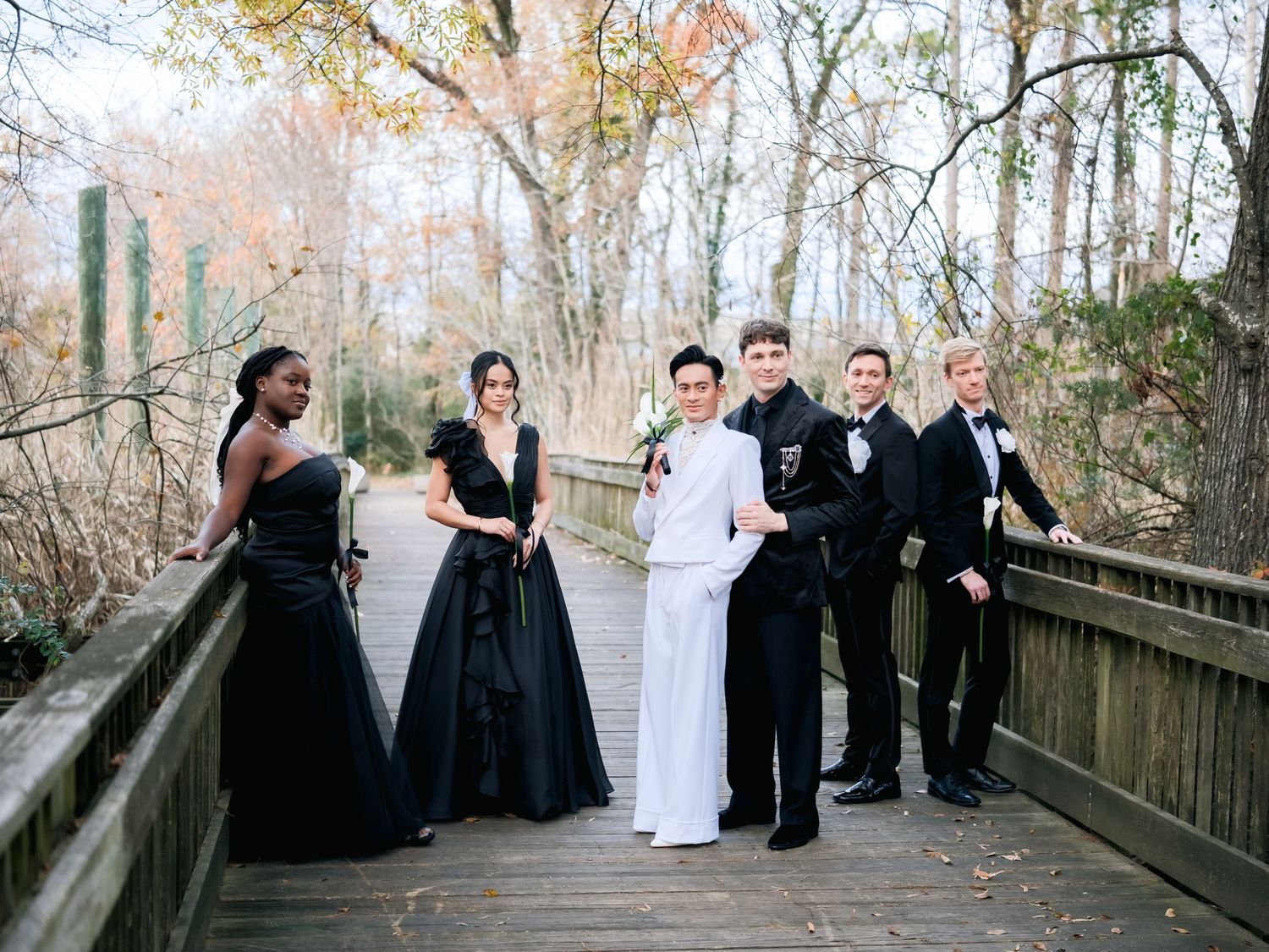 Wedding party poses on wooden bridge in autumn wearing black and white formal attire.