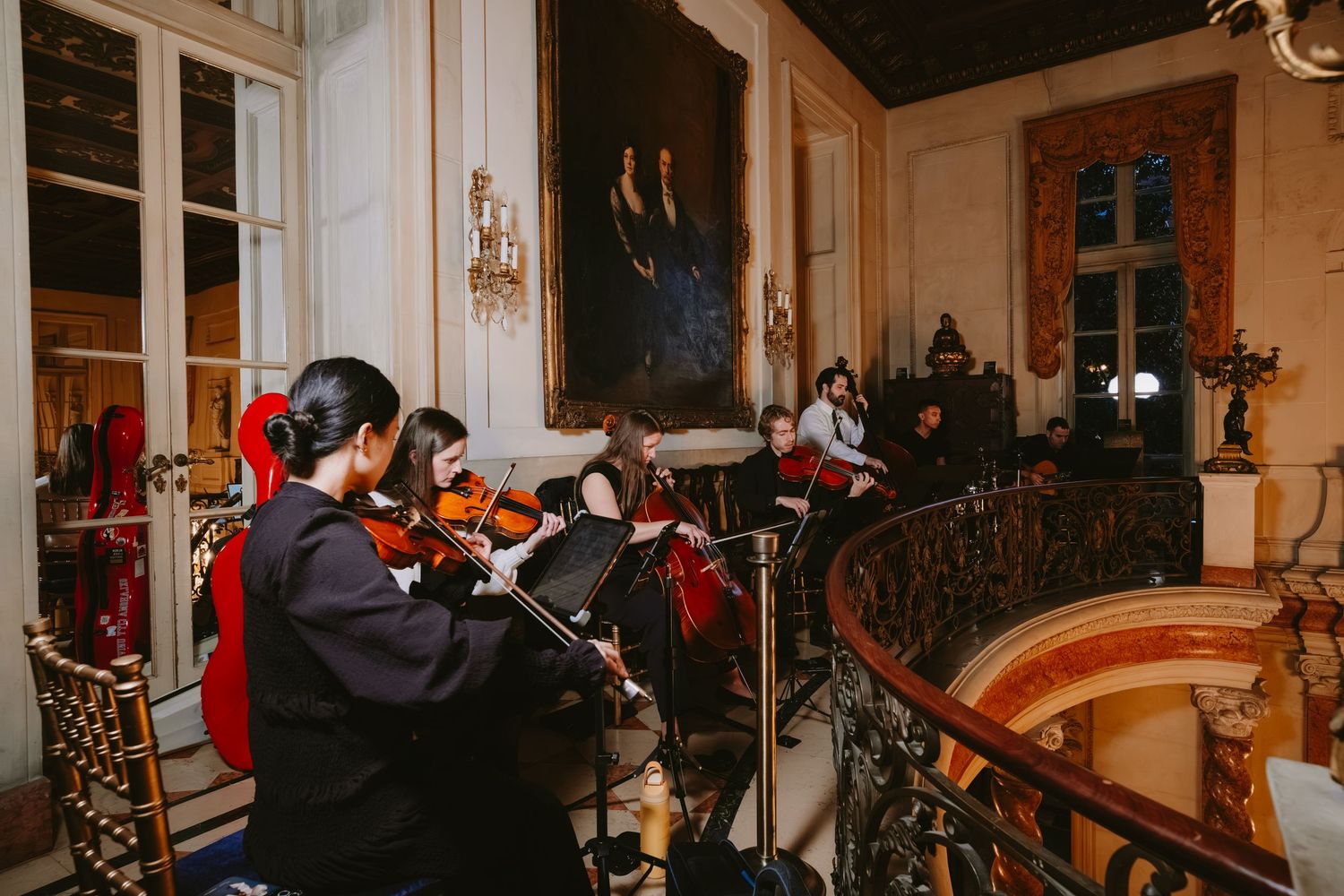 Musicians perform classical music in an elegant ballroom with ornate decor and chandeliers.