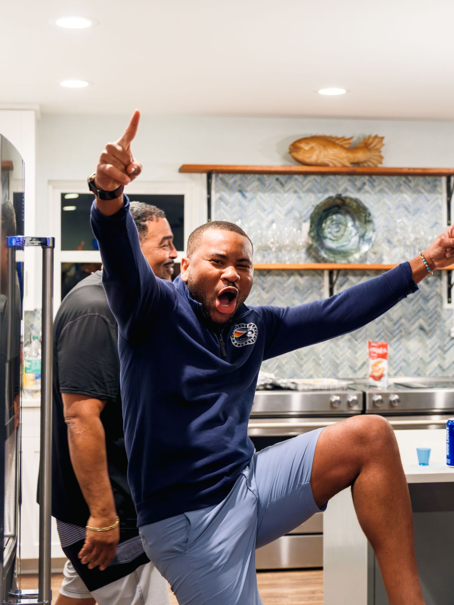 Person in a navy sweater demonstrates high kicks and stretching poses in sequence against a light-colored kitchen background.