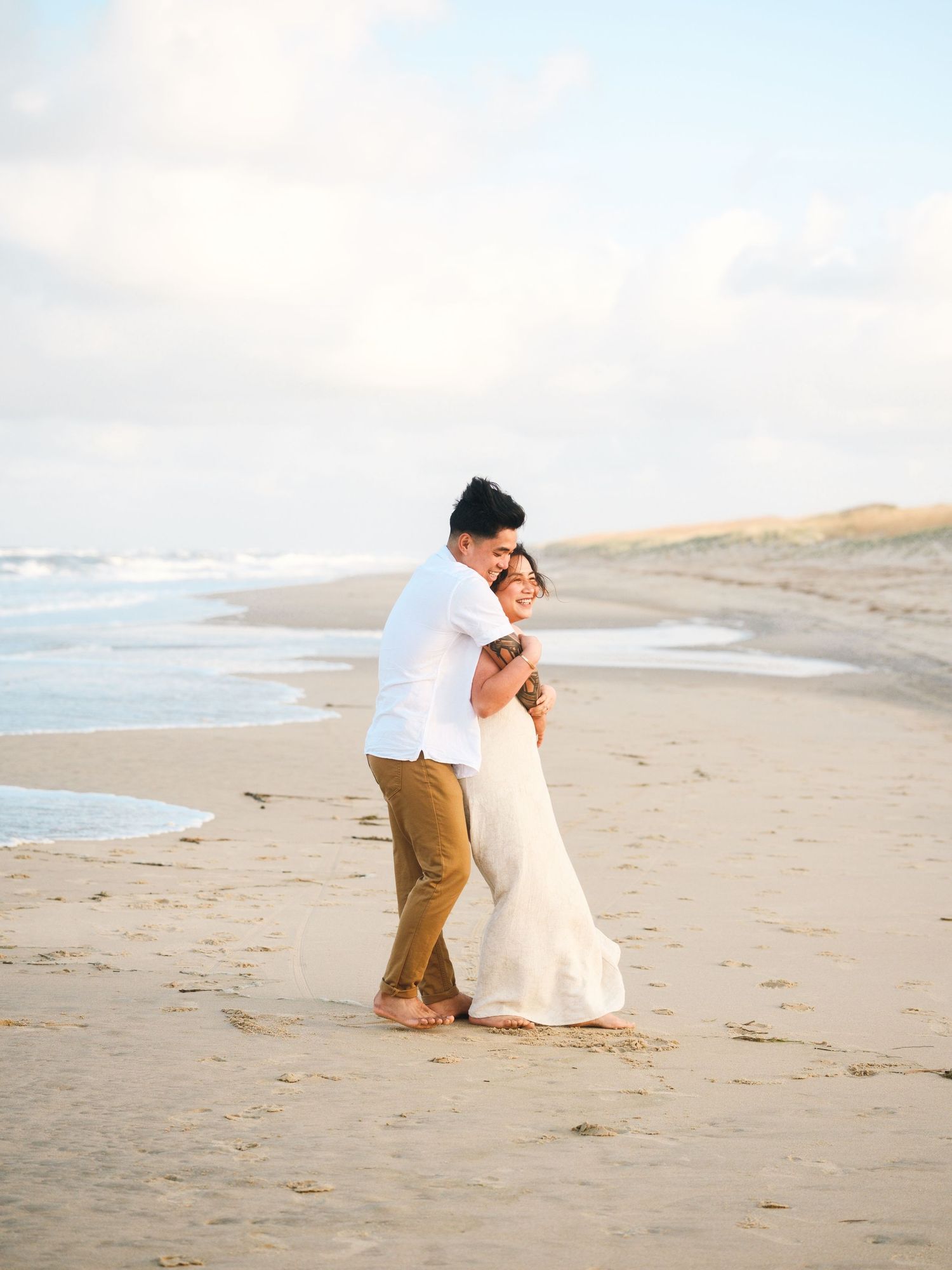A couple in wedding attire share romantic moments while walking along a peaceful beach at sunset.