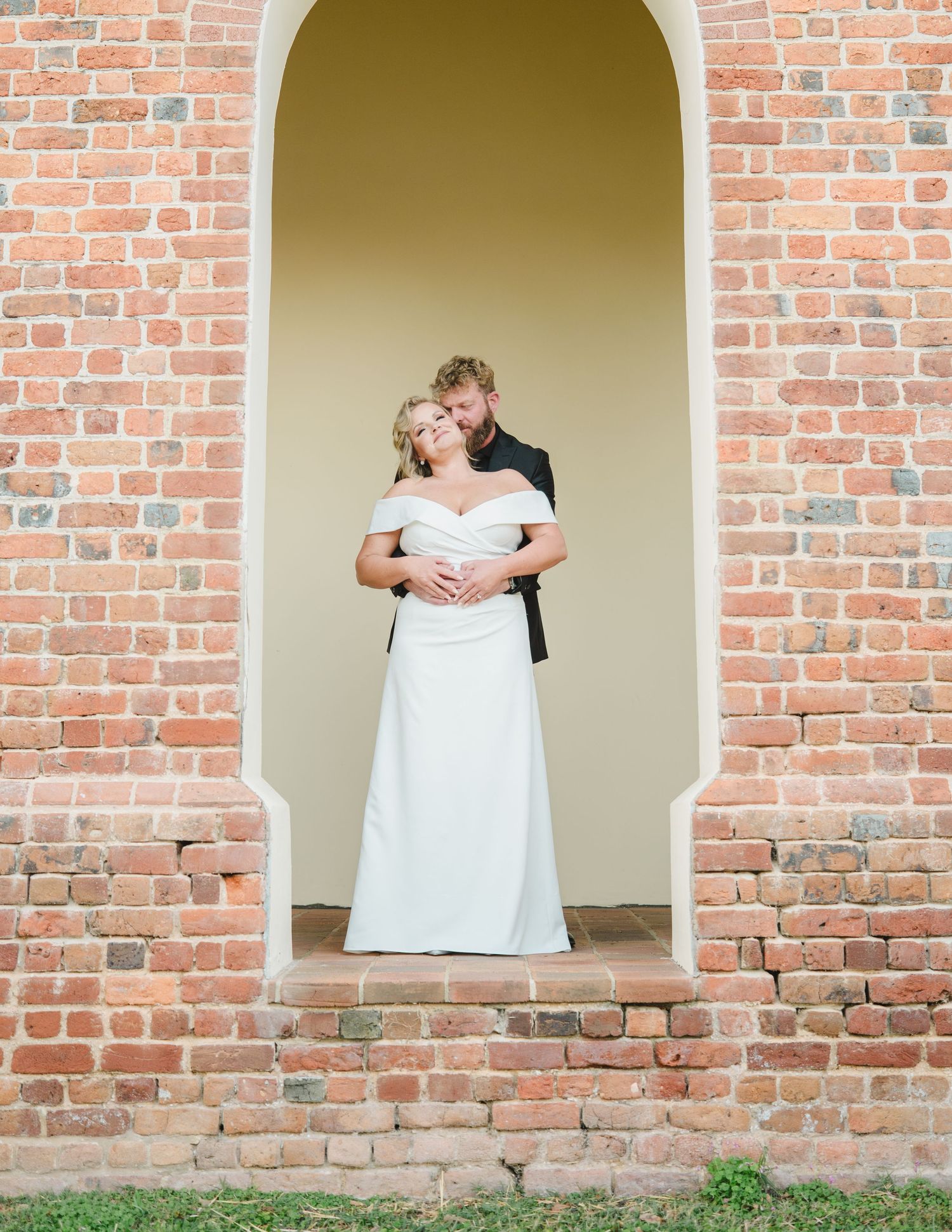 A romantic wedding moment captured through a series of arched brick windows showing a couple embracing on their special day.