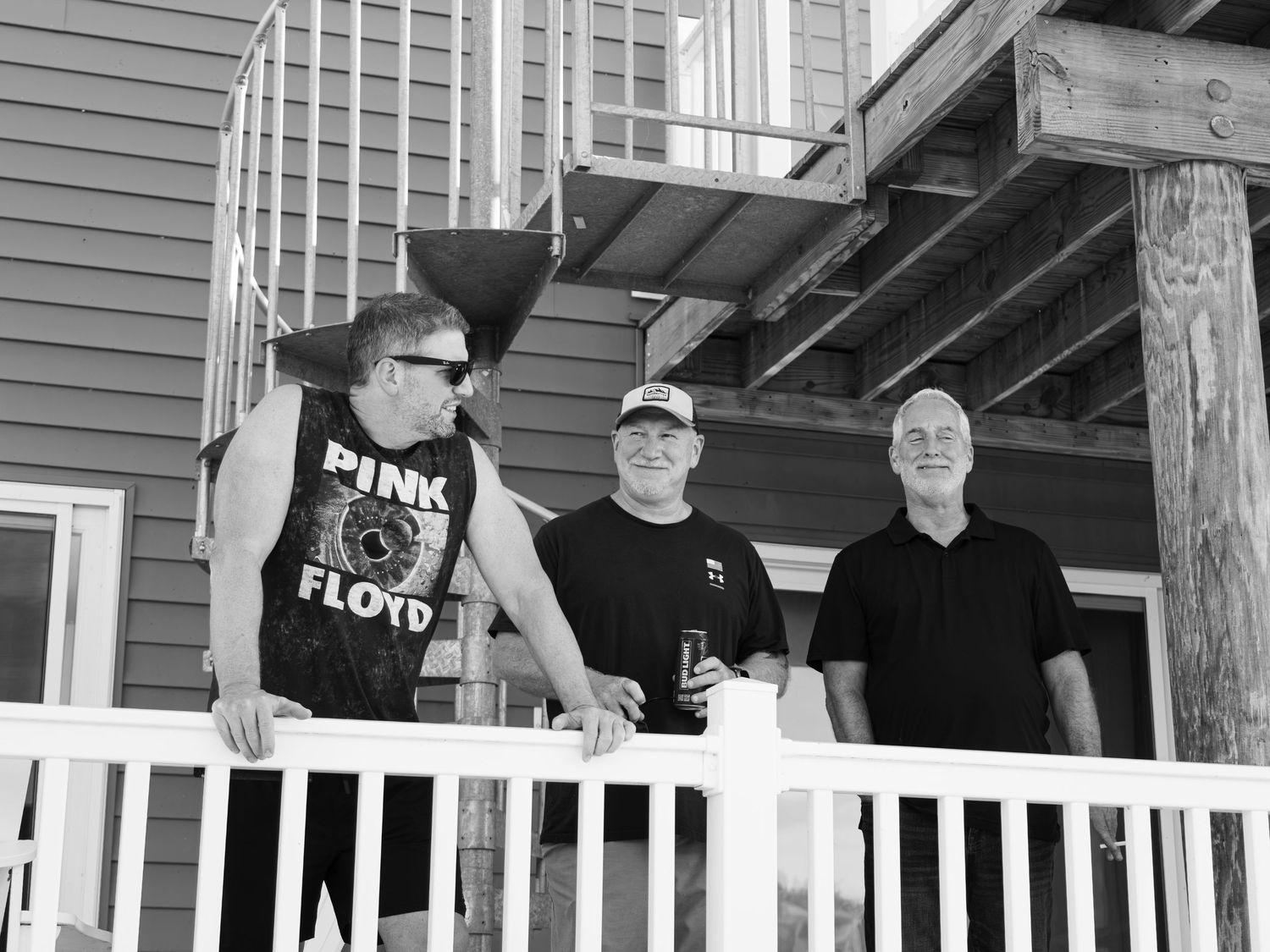 A group of people in black shirts stand together on a covered porch of a residential building.