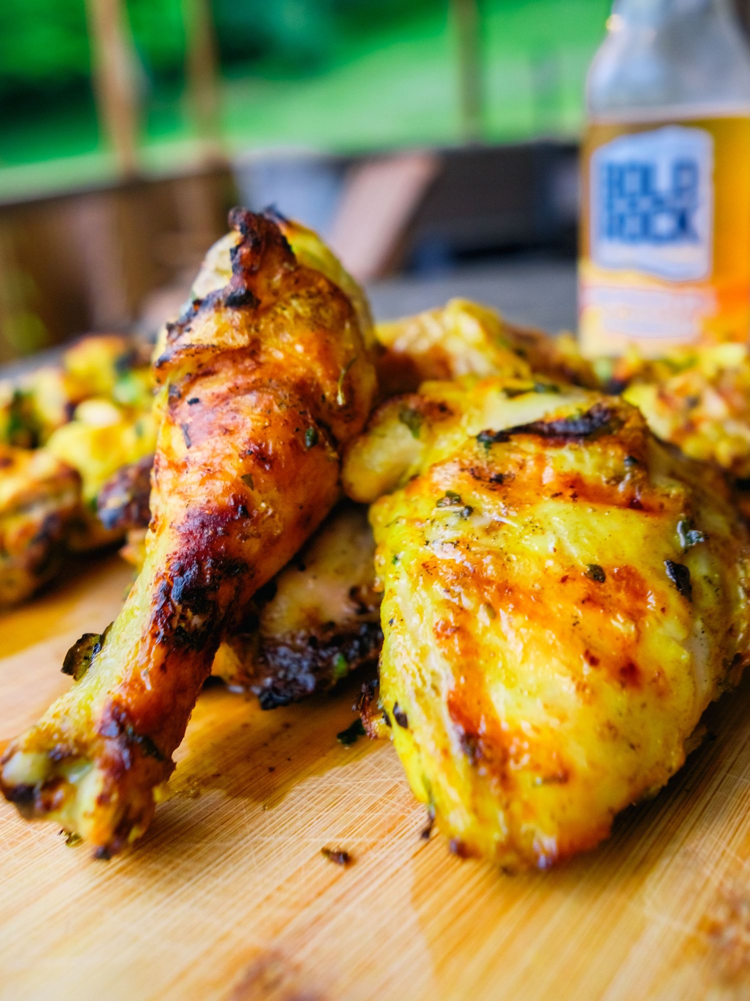Juicy grilled chicken legs with crispy charred skin and yellow marinade served on a wooden cutting board.