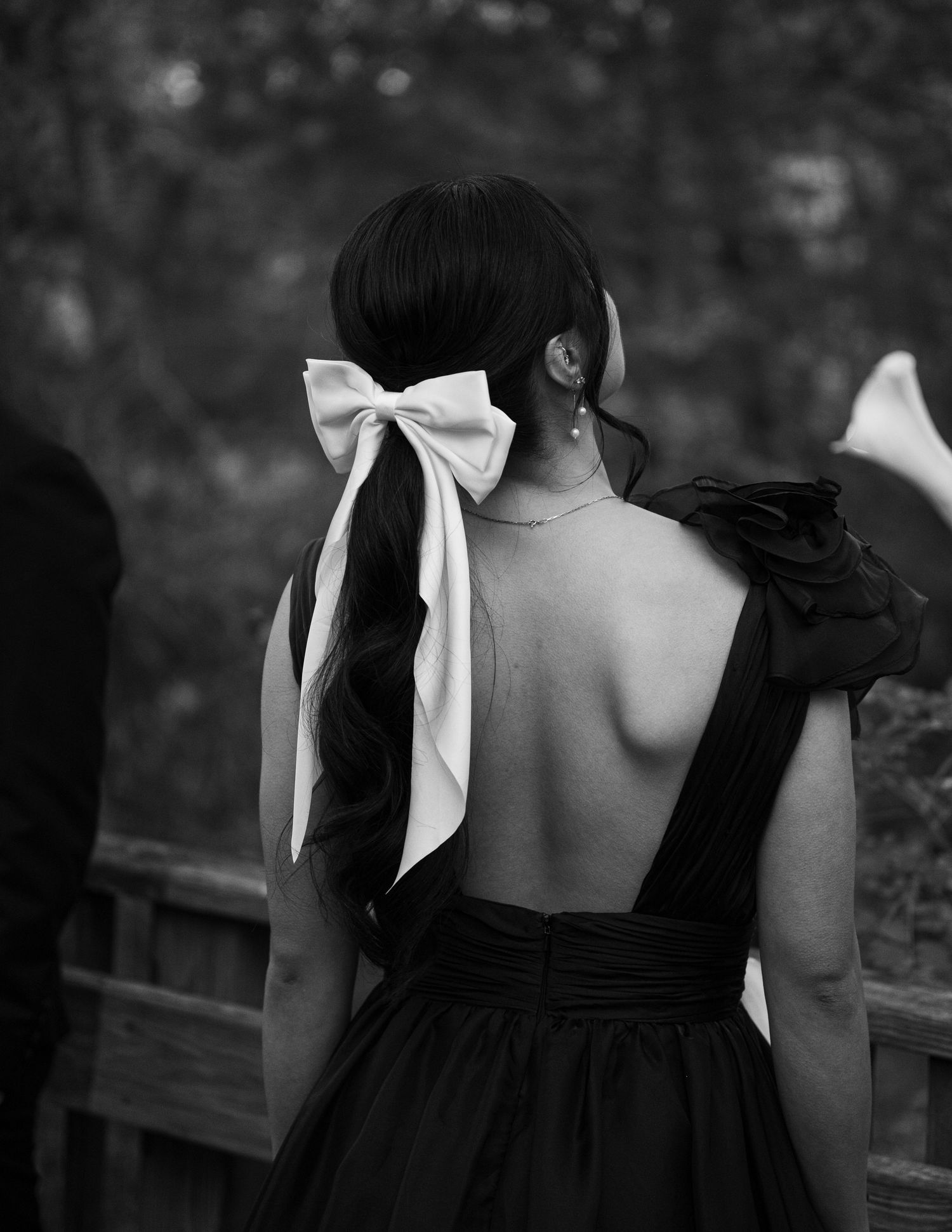 Black and white photo of a person wearing backless dress with large white bow in their dark hair viewed from behind.