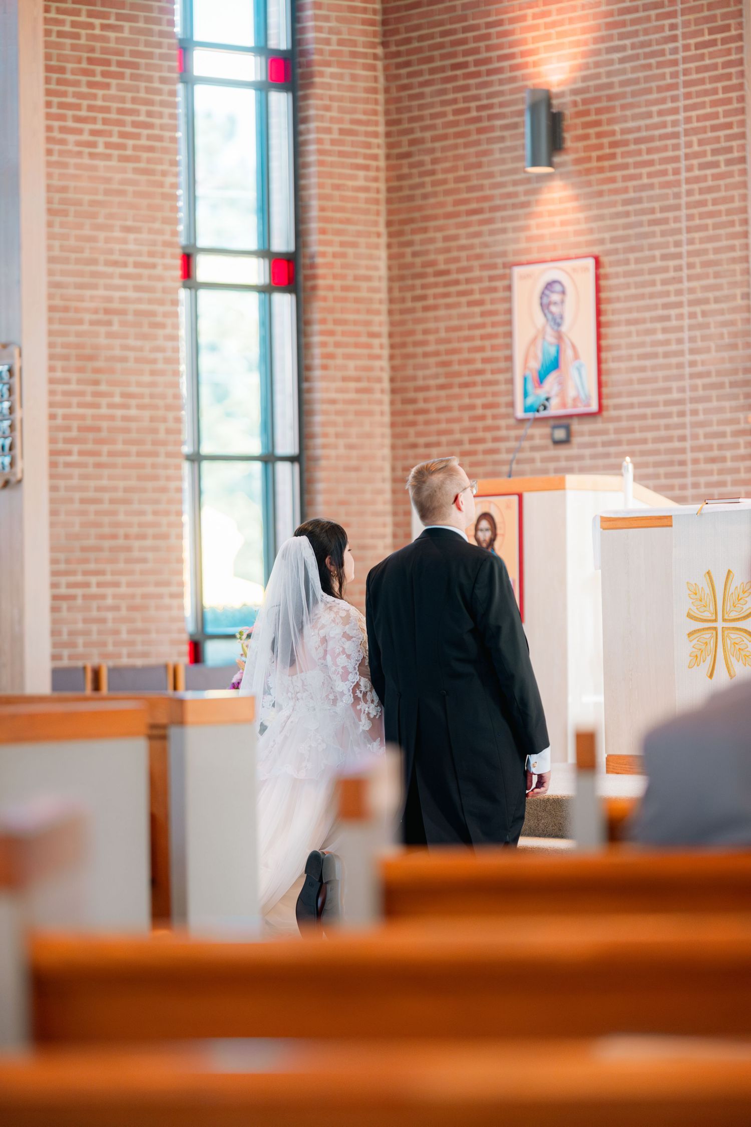 A couple stands at the altar during their wedding ceremony in a church with brick walls and stained glass windows.