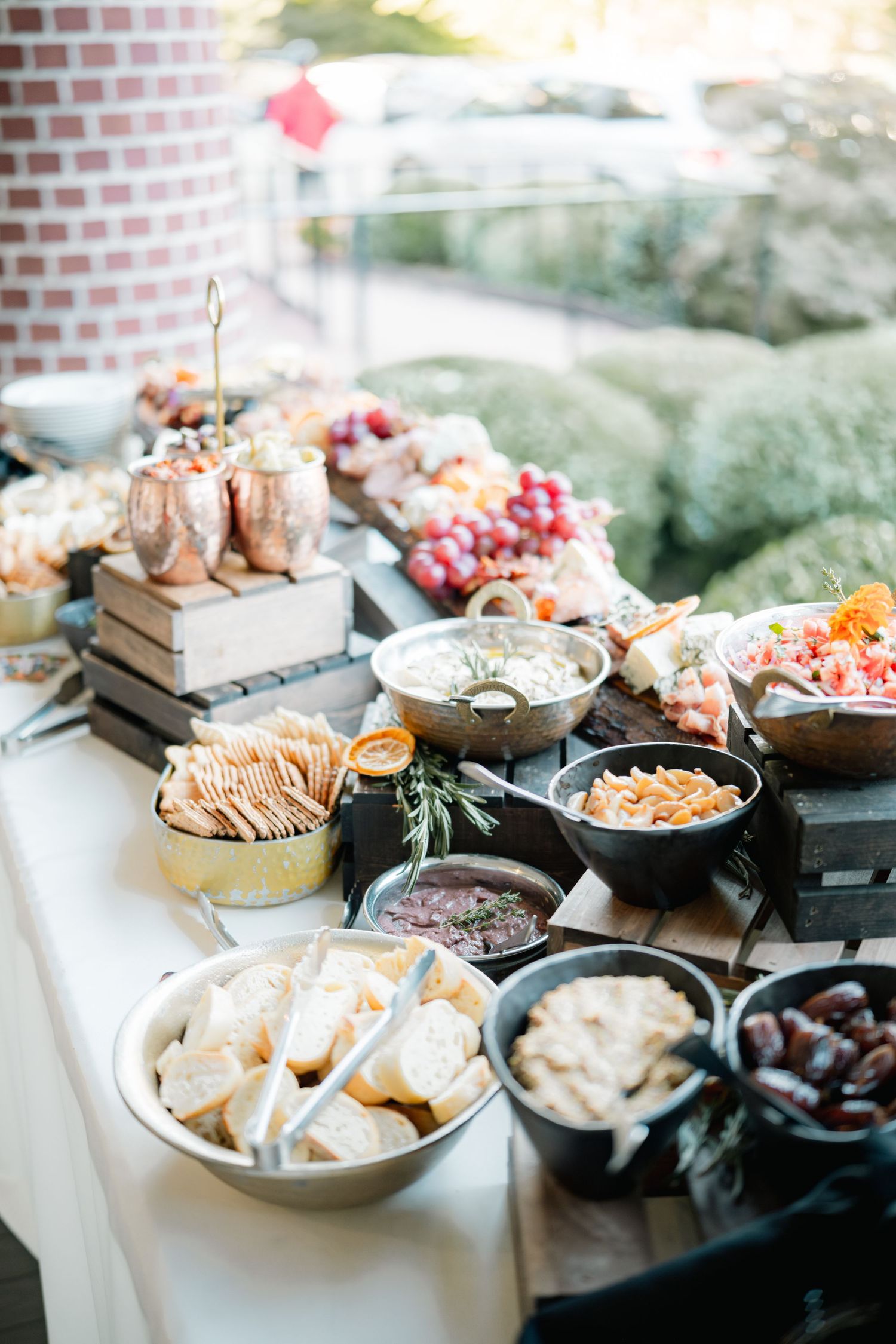 Several bowls of appetizers and snacks laid out on a dark tablecloth against a rustic brick wall.