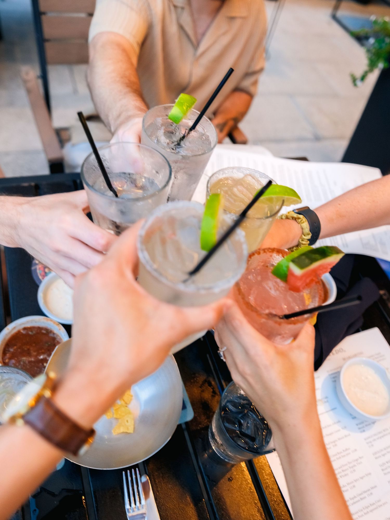 Friends toasting with refreshing cocktails garnished with lime wedges at a restaurant table.