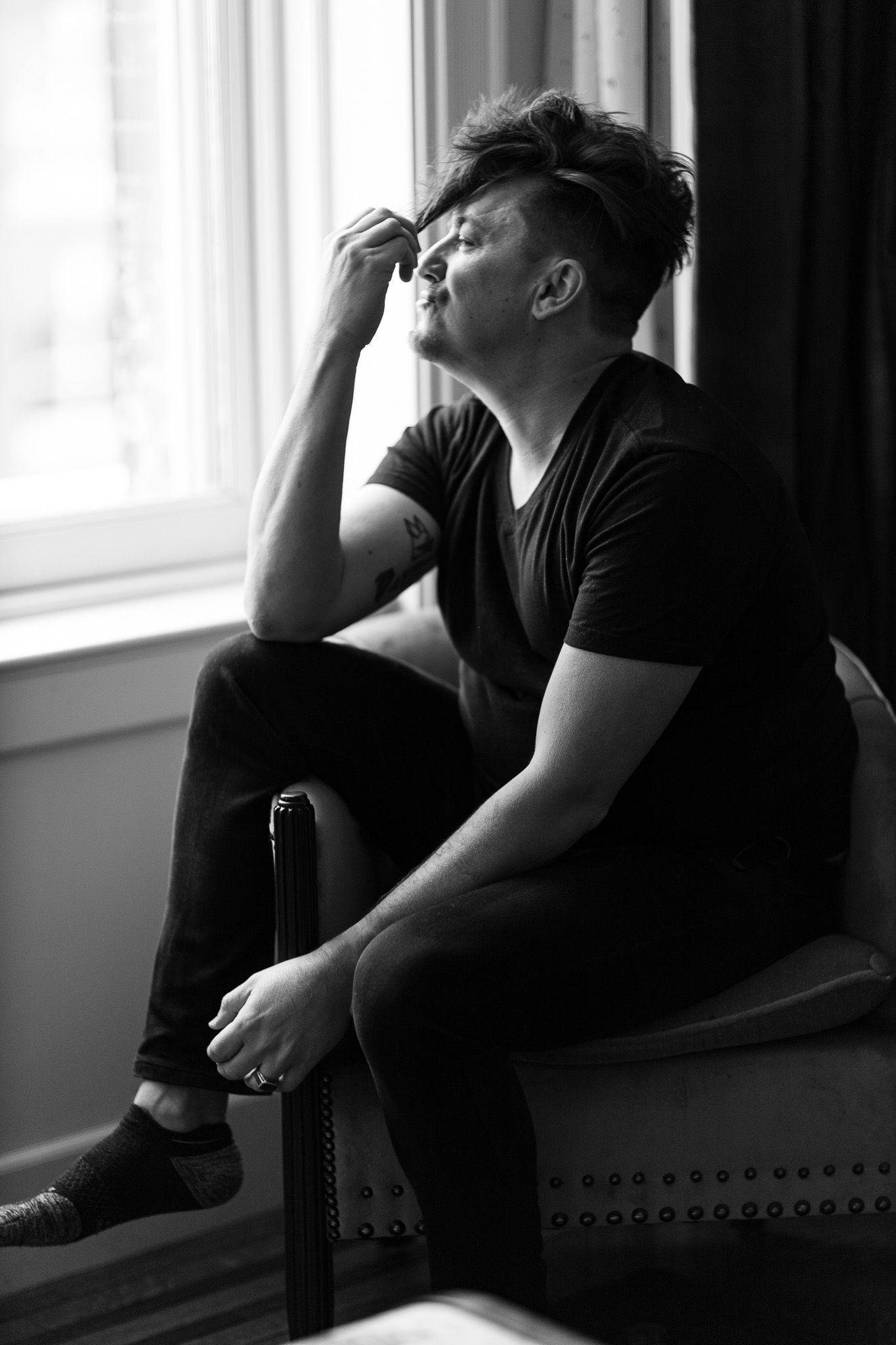 Black and white image showing someone appearing depressed sitting on a couch by a window in low light.