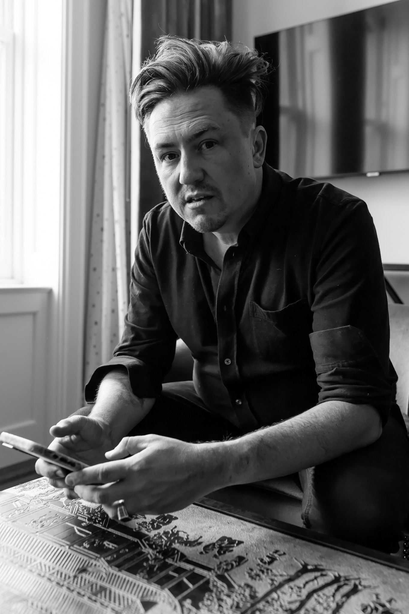 Black and white portrait of person in dark shirt looking pensive while sitting at table.